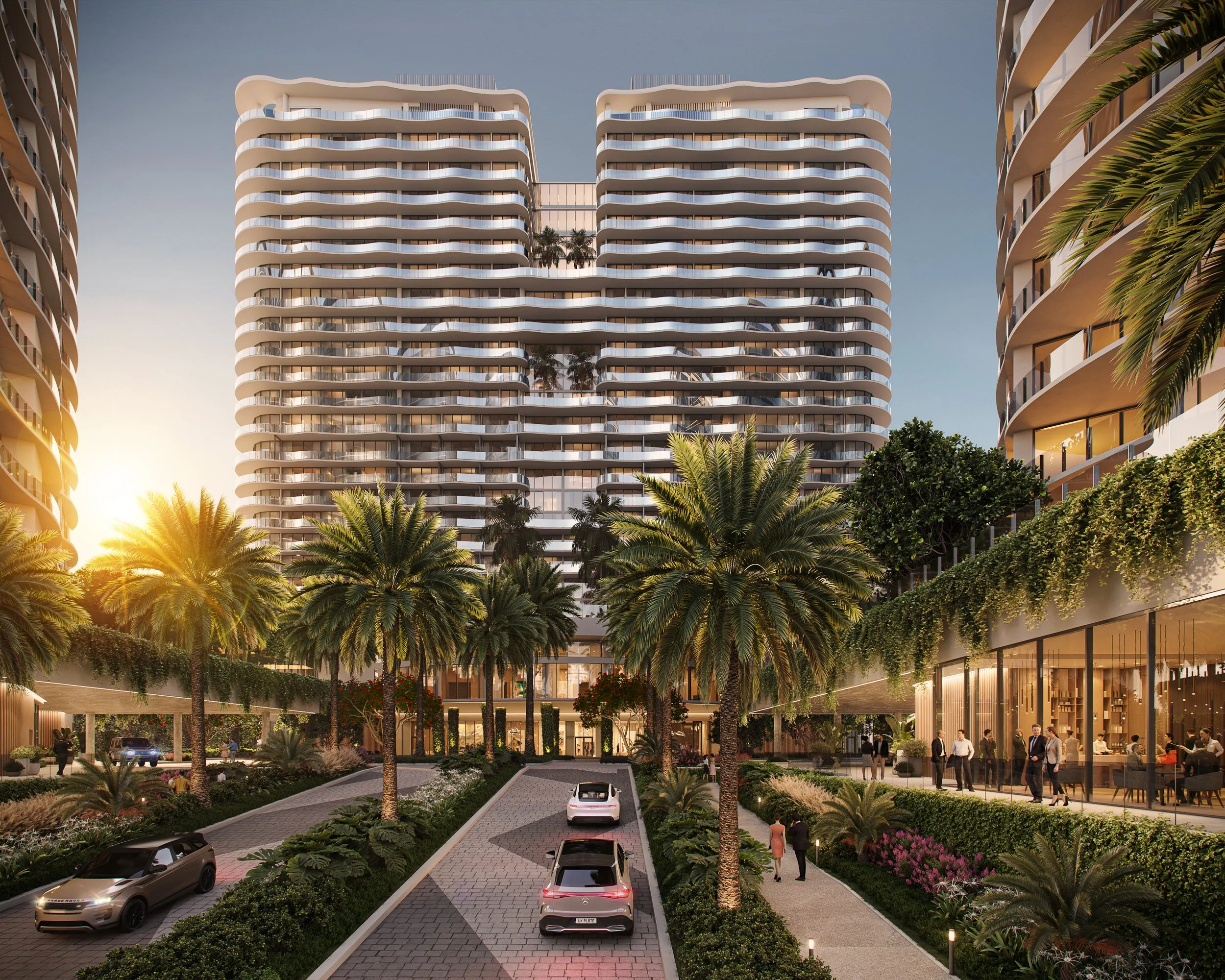 Modern high-rise building with curved balconies, surrounded by palm trees and lush greenery, with people walking and cars parked on the driveway at sunset.