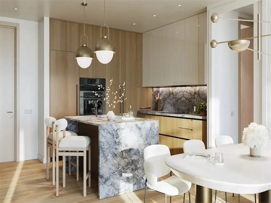 Modern kitchen with marble island, beige cabinetry, and wooden wall panels. White dining table with chairs, decorative flowers, and pendant lighting.