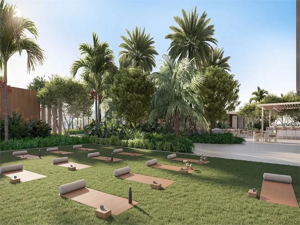 Outdoor yoga area with mats, bolster cushions, and yoga blocks on a grassy lawn surrounded by palm trees and lush greenery.