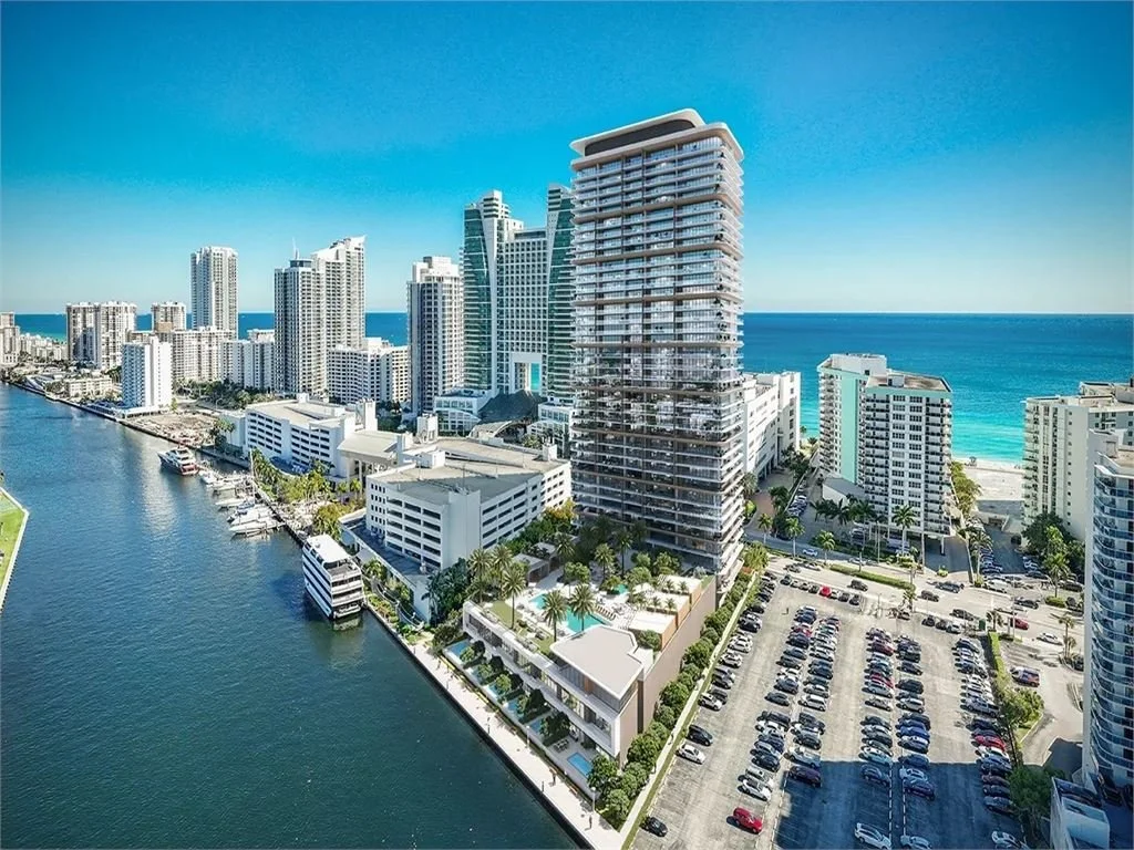 High-rise buildings near a waterway with a parking lot in the foreground, overlooking the ocean in the distance
