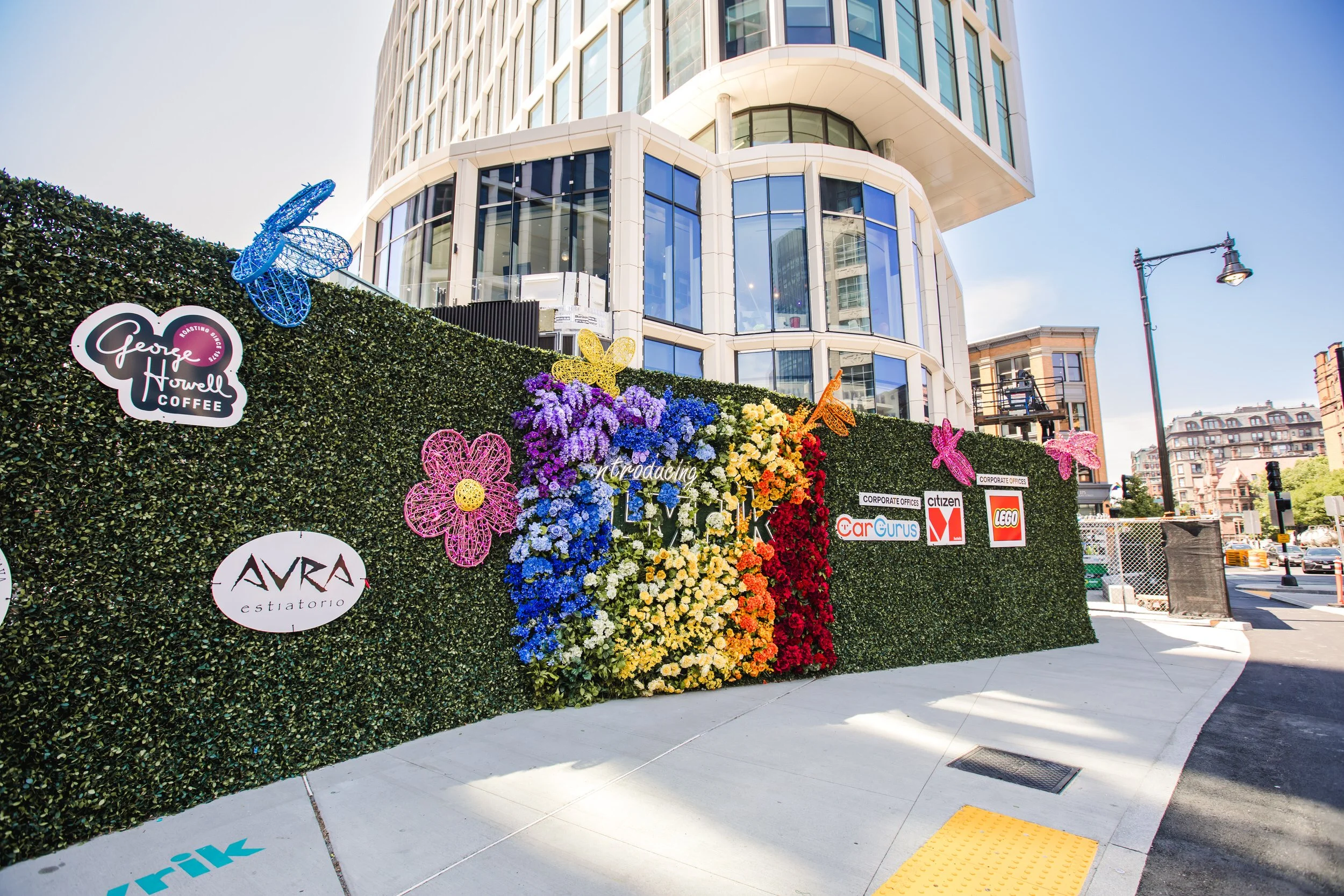  A colorful floral arrangement and small signs hanging on a fence covered in greenery 