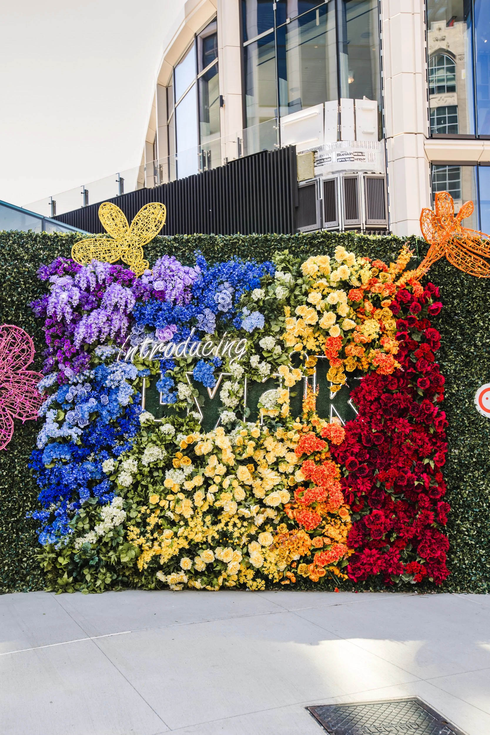  A rainbow colored floral arrangement on a fence covered in greenery  