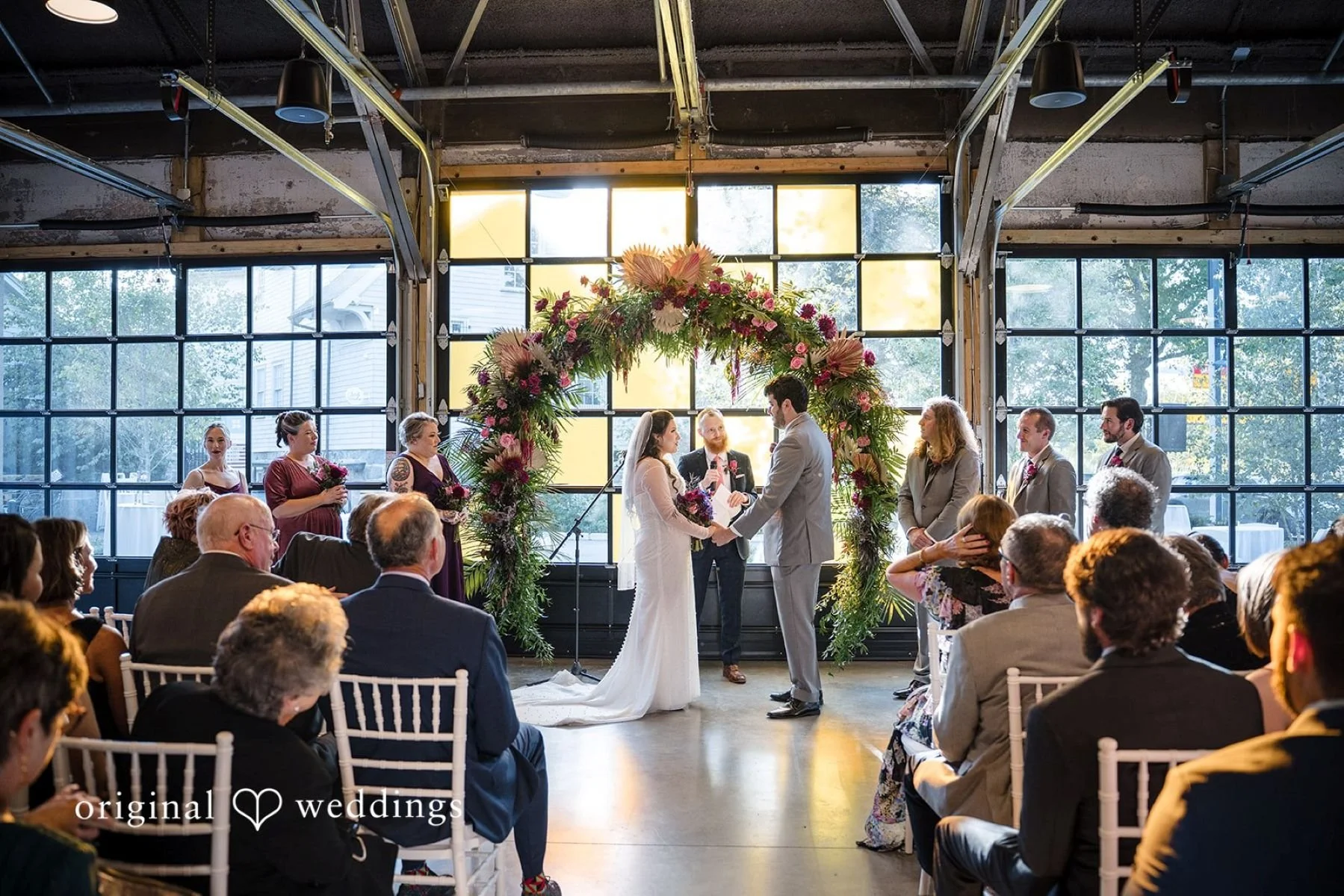 a couple having their wedding in front of a floral installatoin in garage b