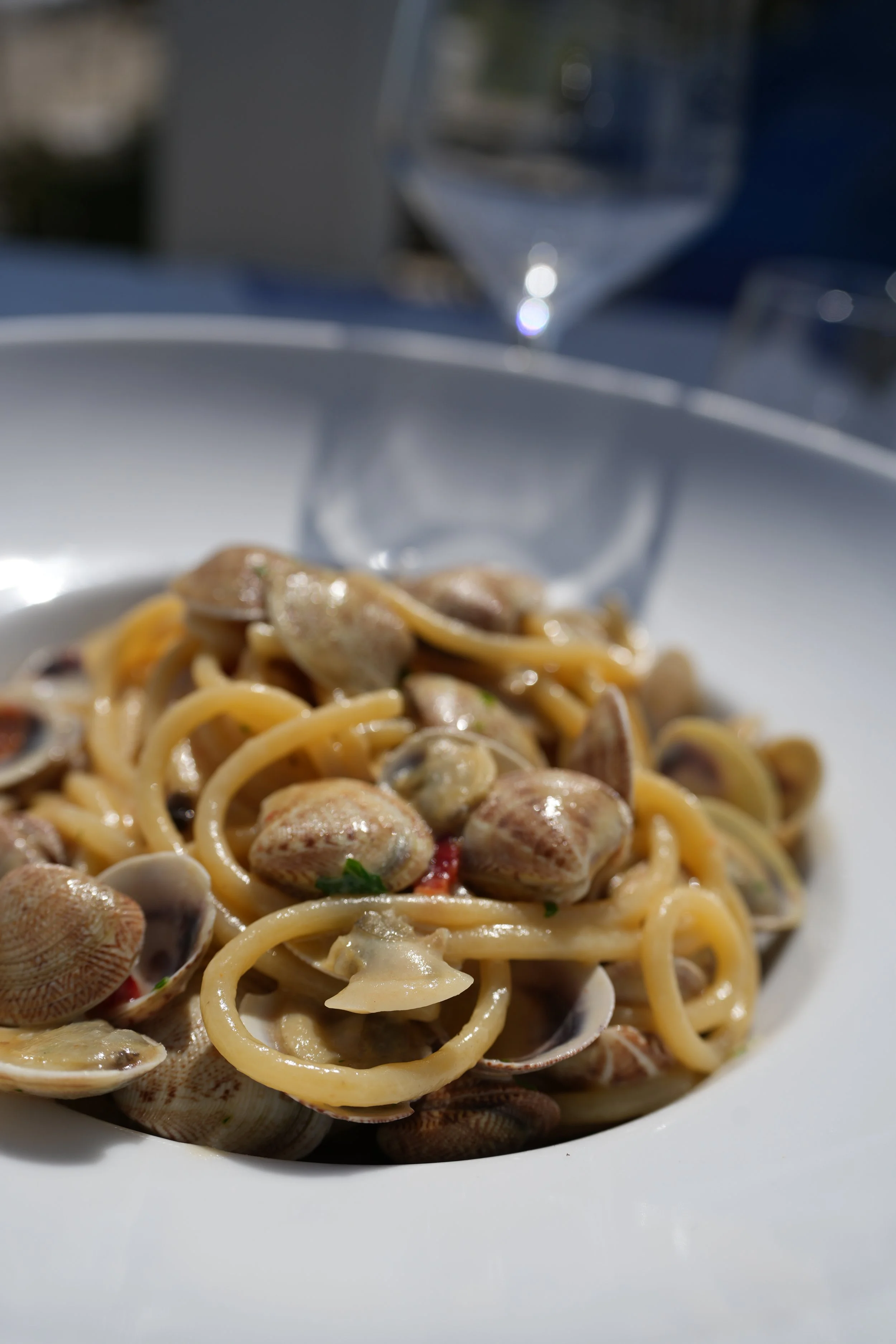 Piatto di spaghetti alle vongole con prezzemolo, vicino a un bicchiere di vino bianco