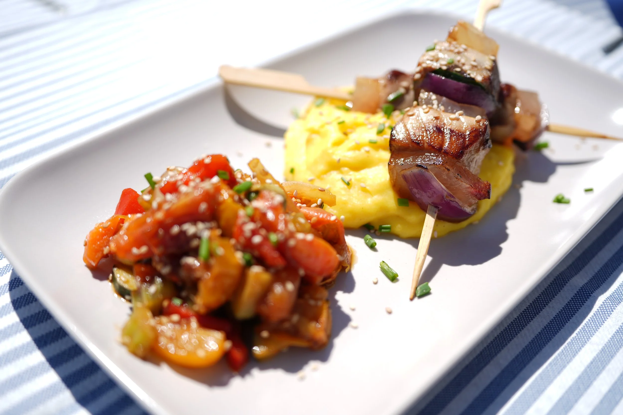 Piatti con verdure, arrosticino di tonno e purè di patate decorati con semi di sesamo e erba cipollina.