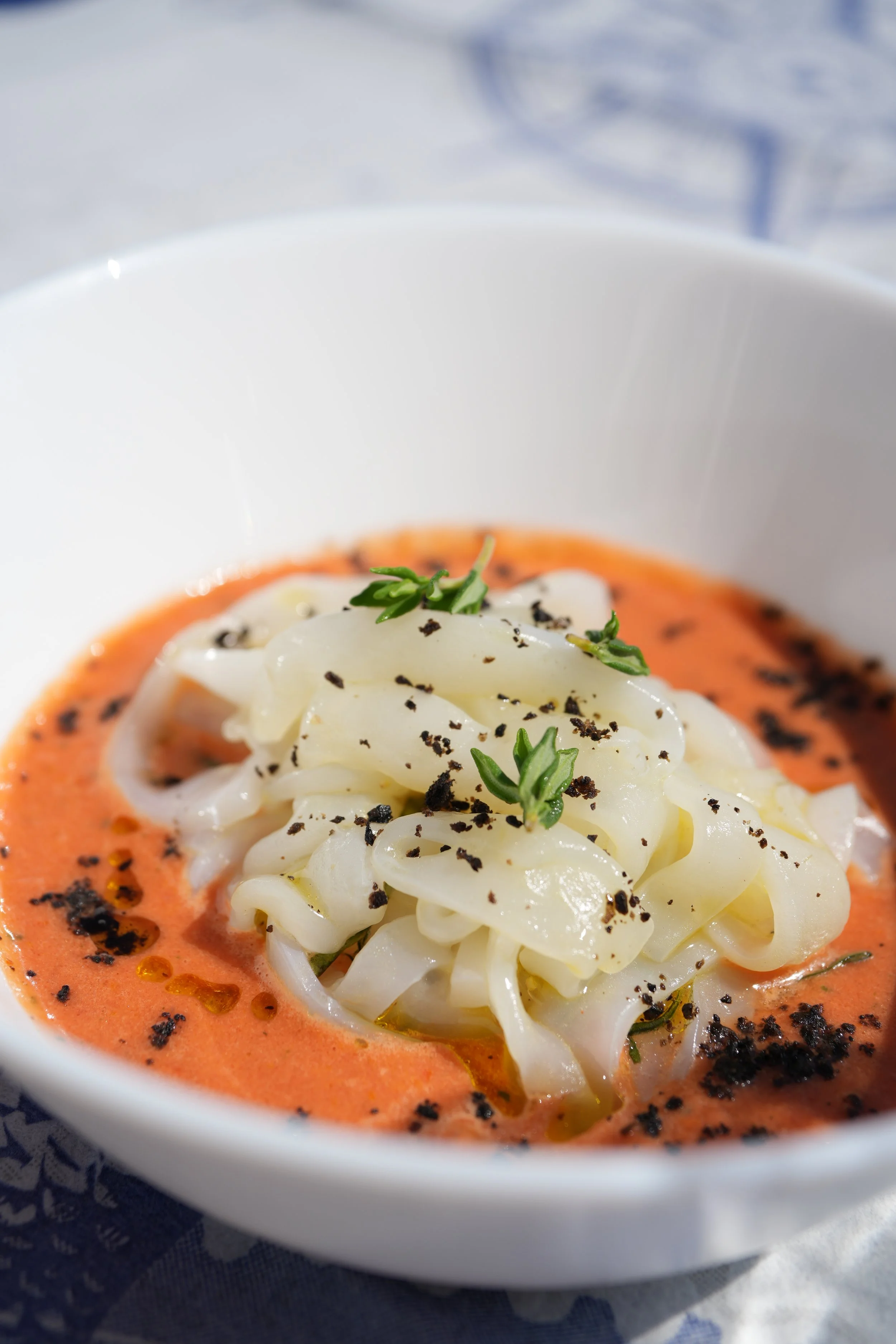 Tagliatelle di seppia con salsa al pomodoro, guarnita con erba aromatica e spezie.