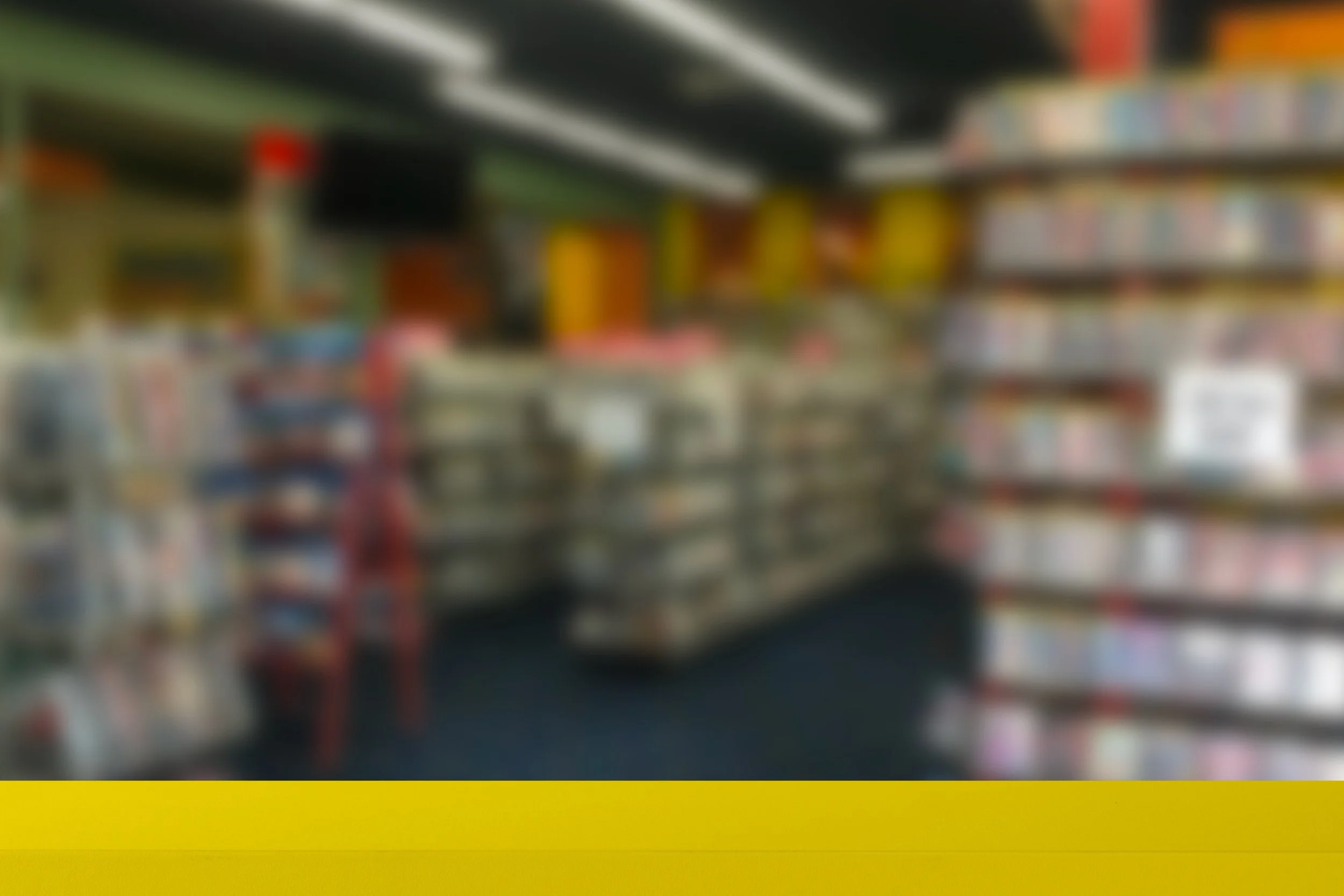 Blurred view of grocery store shelves filled with various products, with a yellow safety line at the bottom.