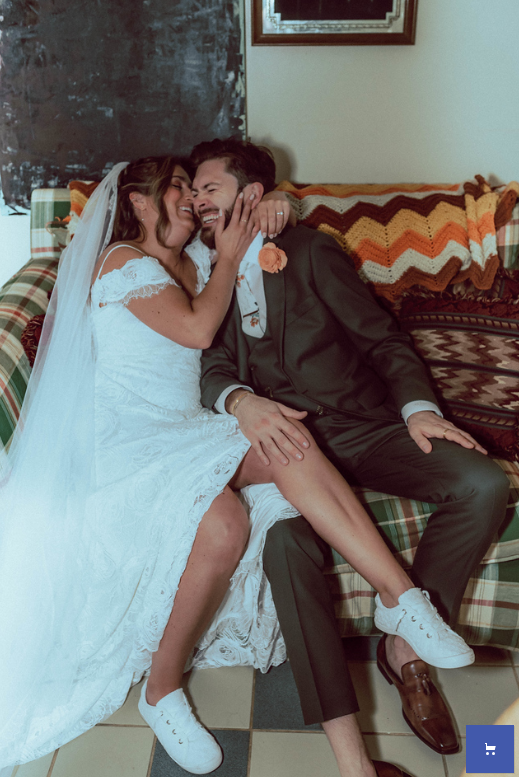 A couple holding hands standing in front of lush plants inside a dark greenhouse or botanical garden at night.