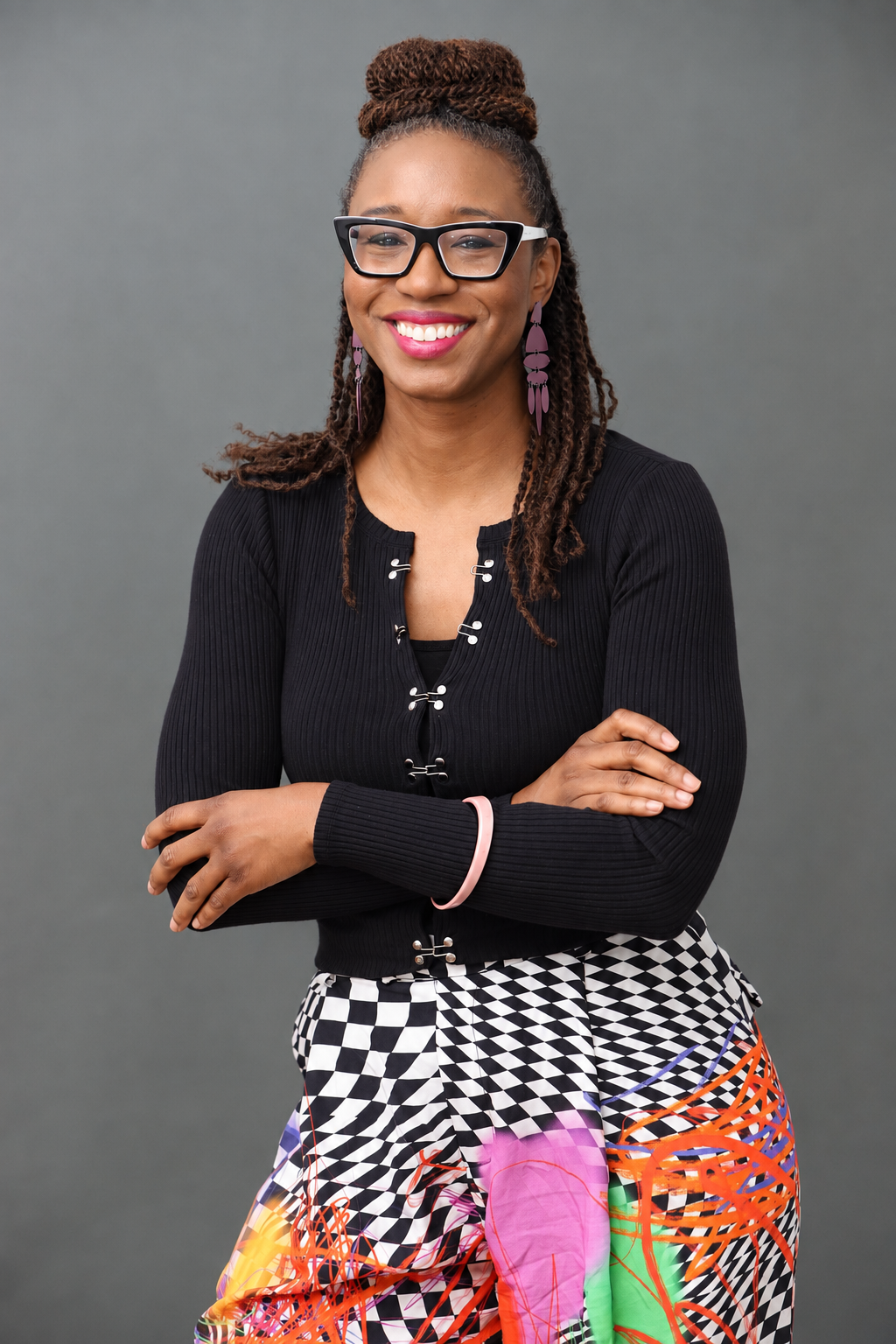 Smiling person with glasses and braided hair, wearing a necklace, black and white photo