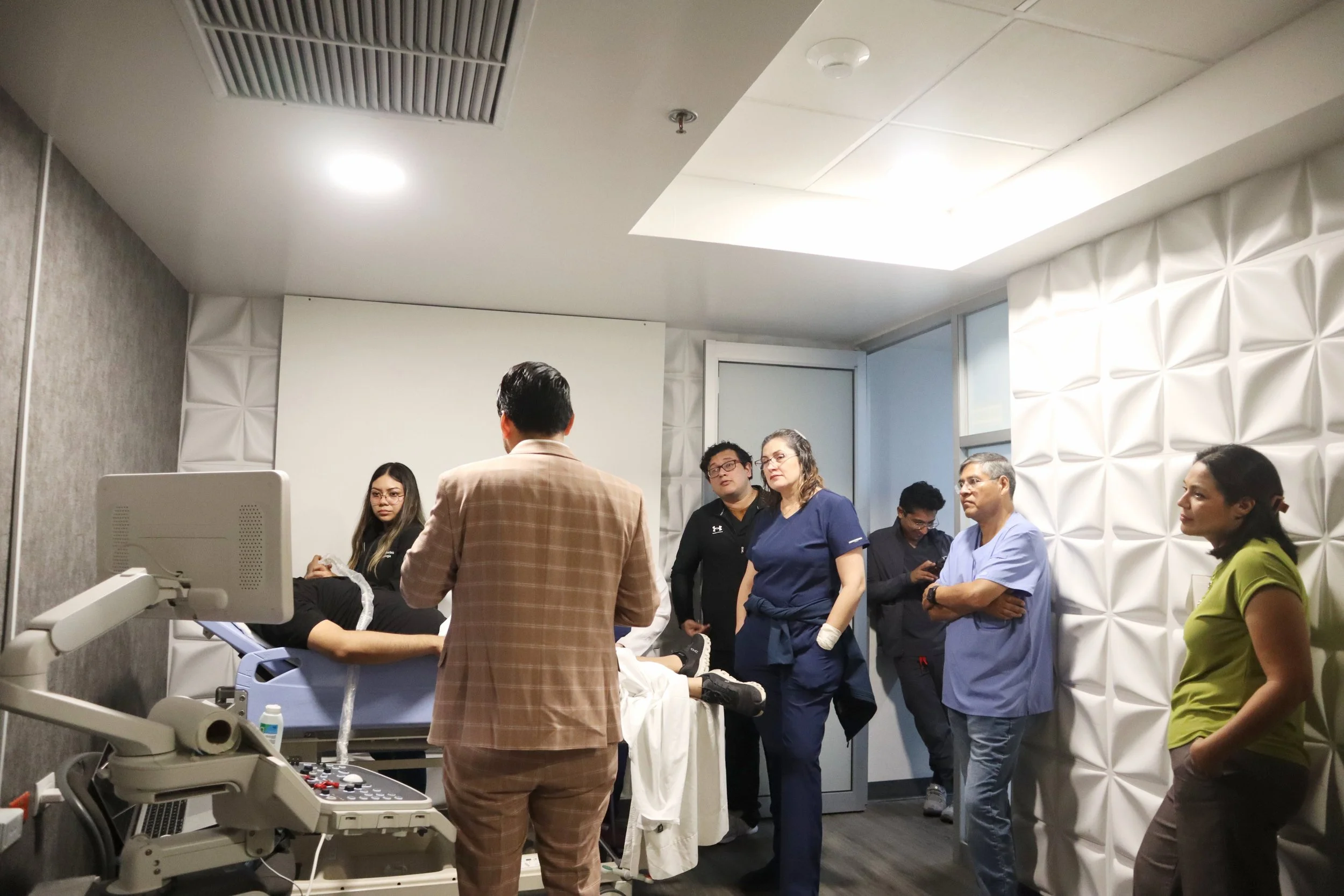 Personal médico y especialista en una sala de emergencias atendiendo a una paciente en una camilla, todos observando y conversando sobre la atención médica. ACÉRCATE Asociación para certificación y capacitación Técnica Catéter PICC