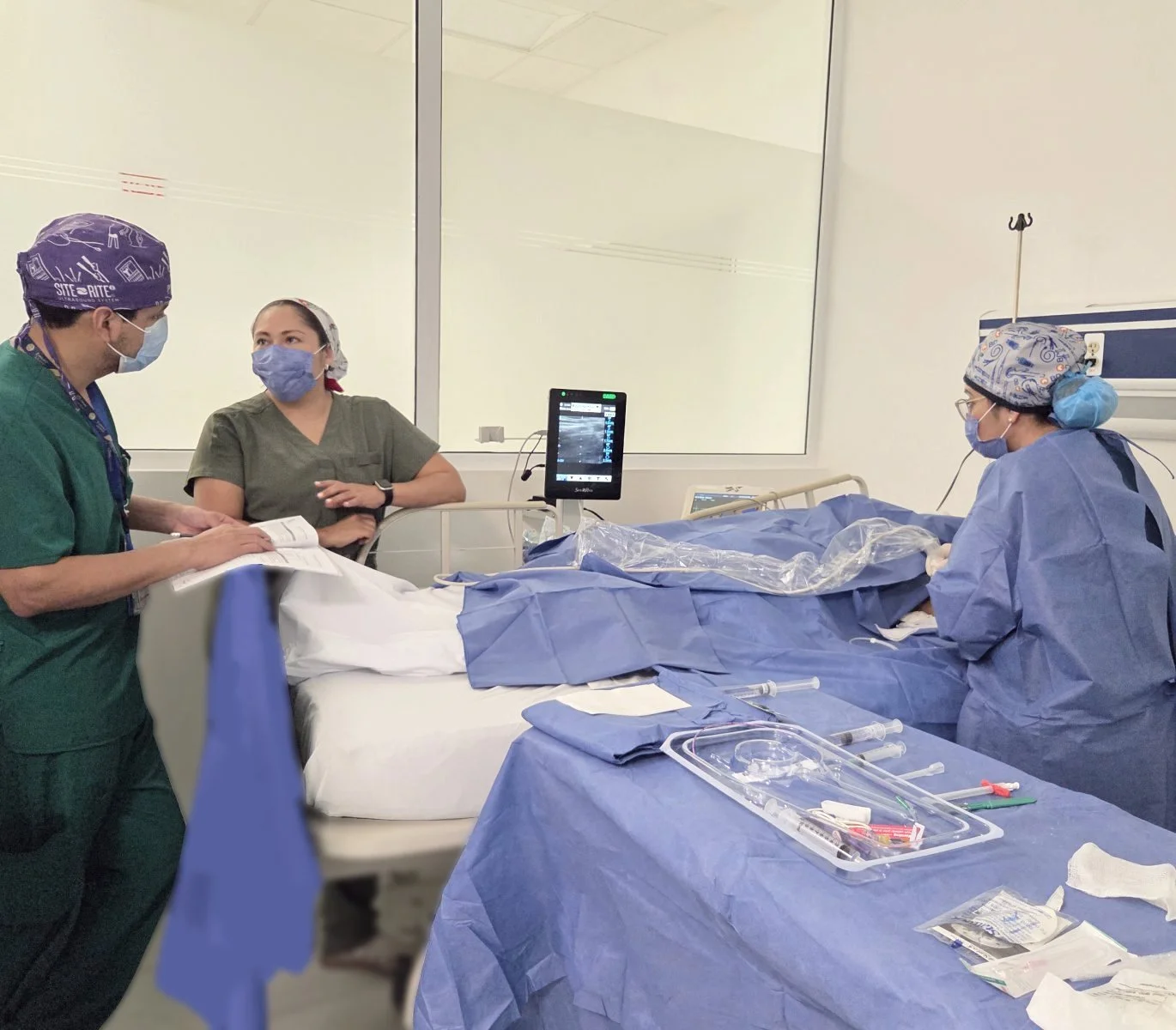 Equipo médico en un quirófano realizando un procedimiento médico, con monitoreo, instrumentos y pacientes en la cama. ACÉRCATE Catéter PICC