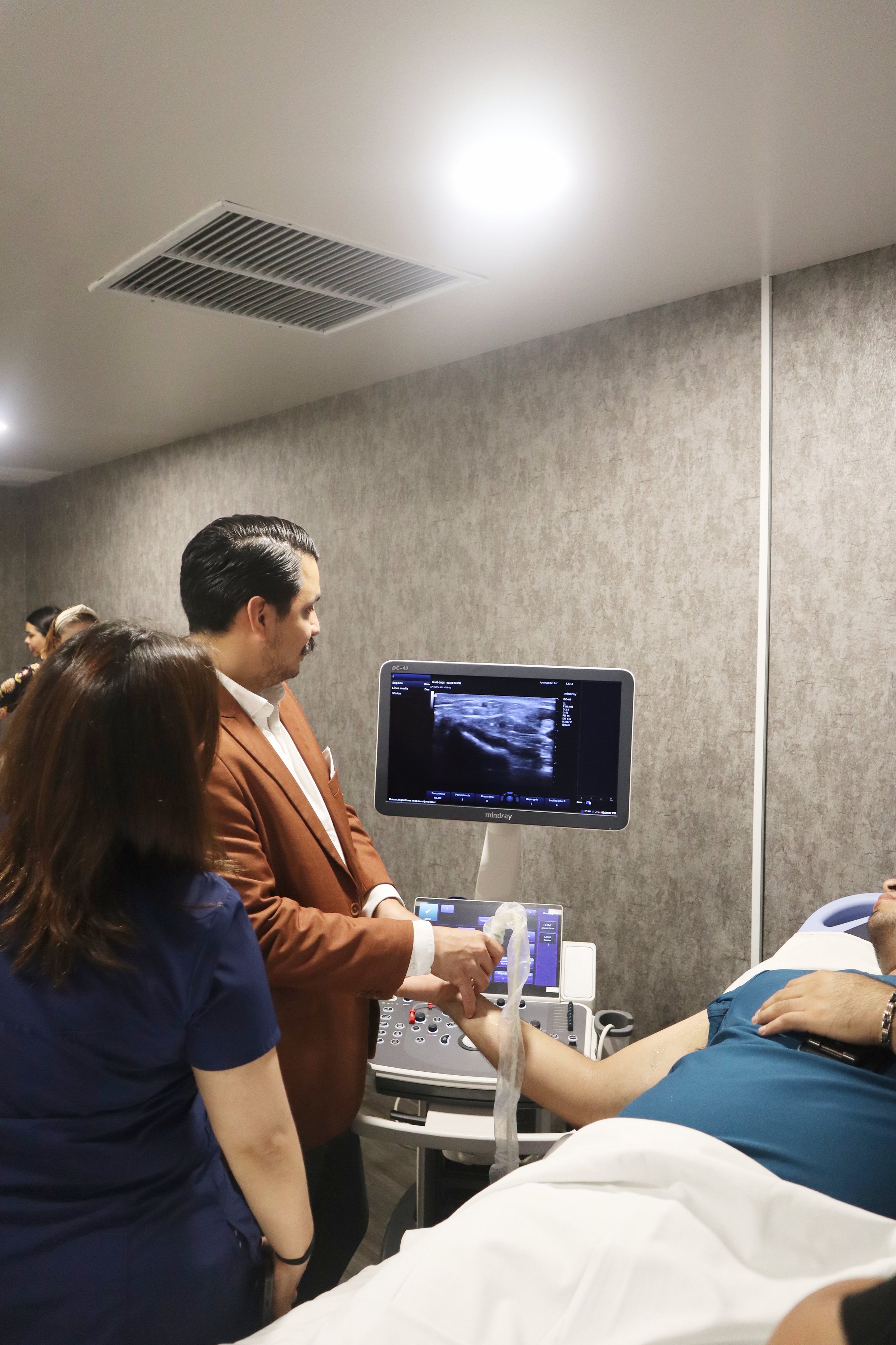 Dos médicos realizan una ecografía a un paciente en una clínica o hospital, mientras observan la pantalla del ultrasonido. ACÉRCATE Asociación para certificación y capacitación Técnica Catéter PICC