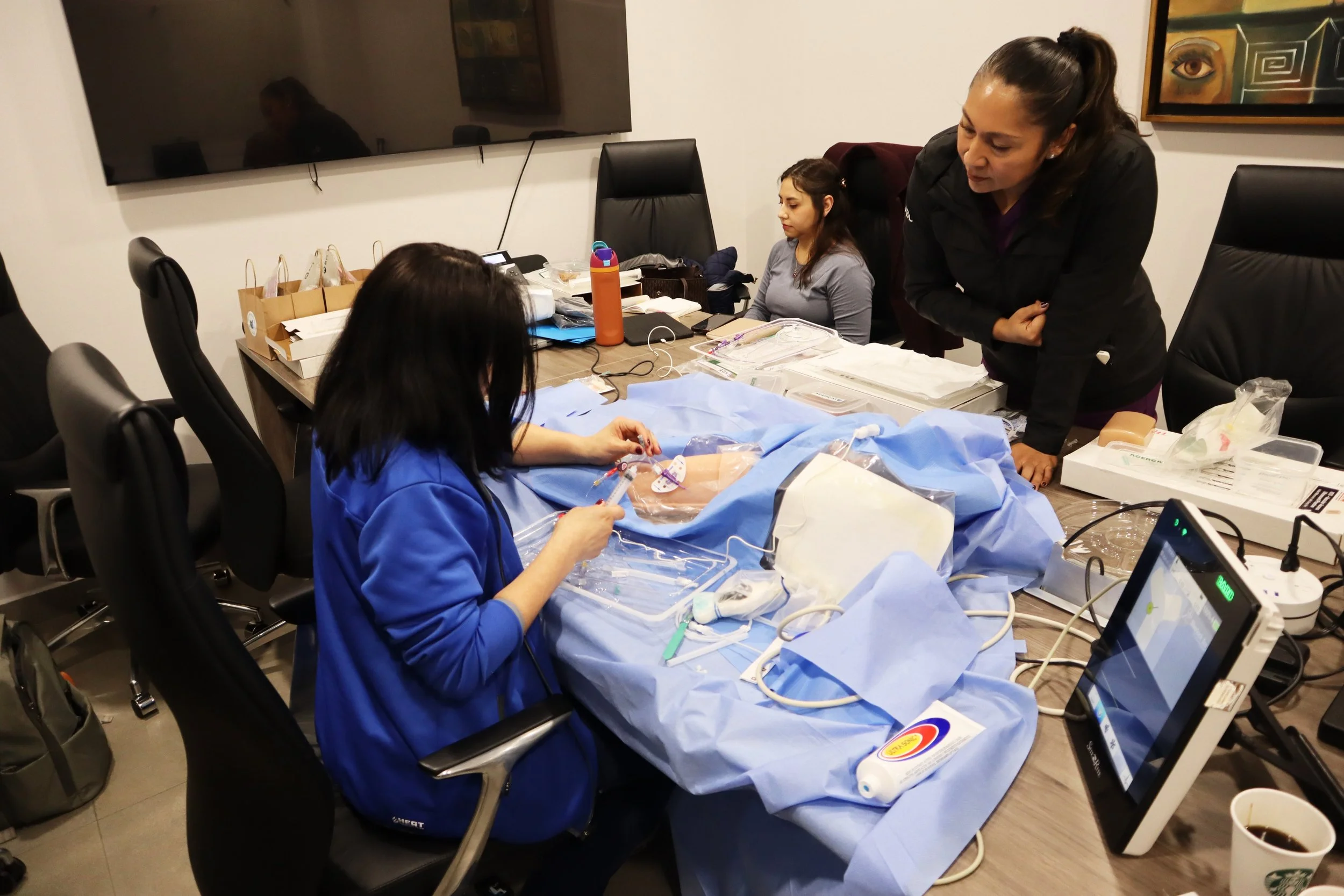 Personal médico atendiendo un bebé en un procedimiento en una sala de hospital, con monitores y equipo médico. ACÉRCATE Asociación para certificación y capacitación Técnica Catéter PICC