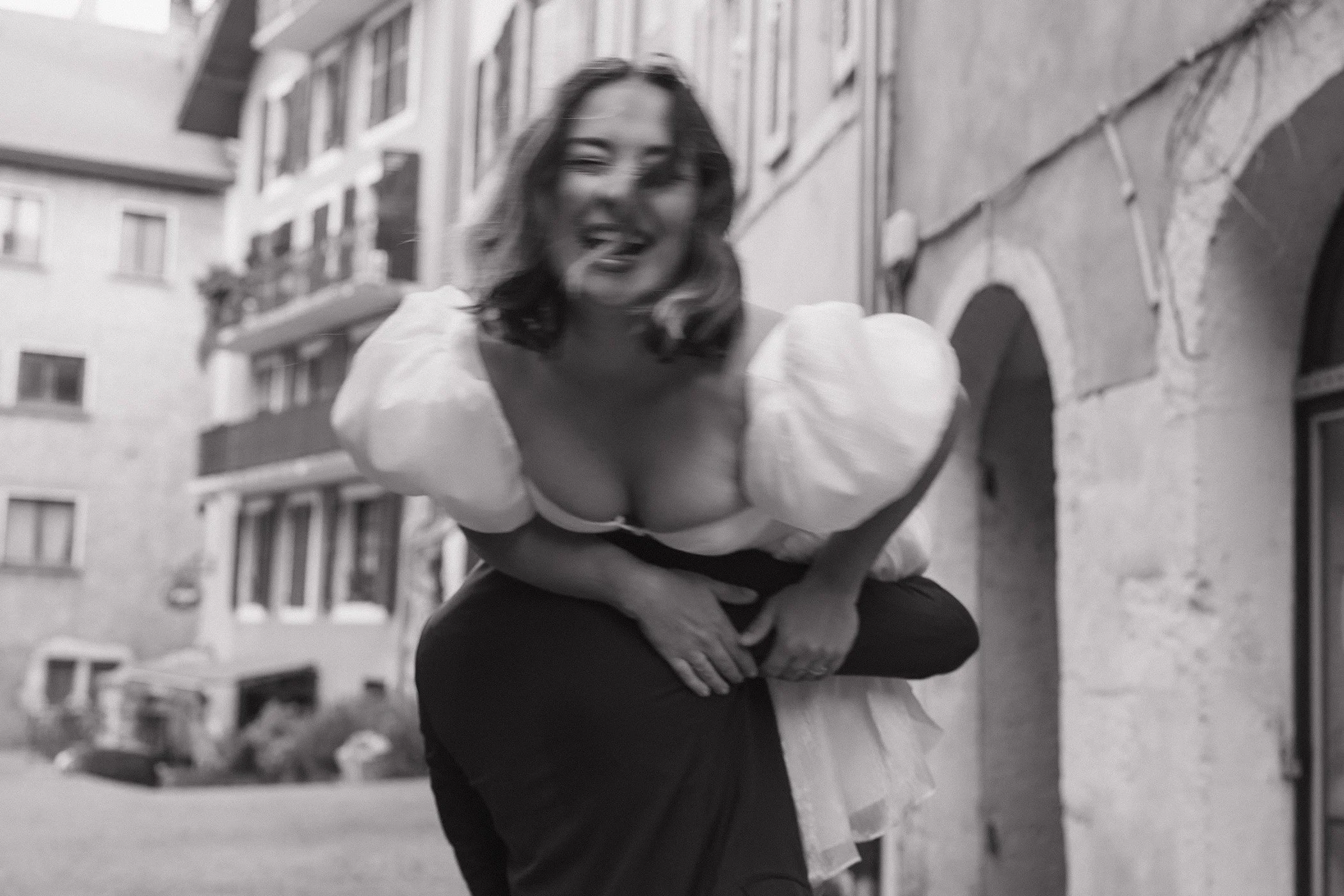 Une mariée éclatant de rire portée par son partenaire dans une ruelle d'Annecy.