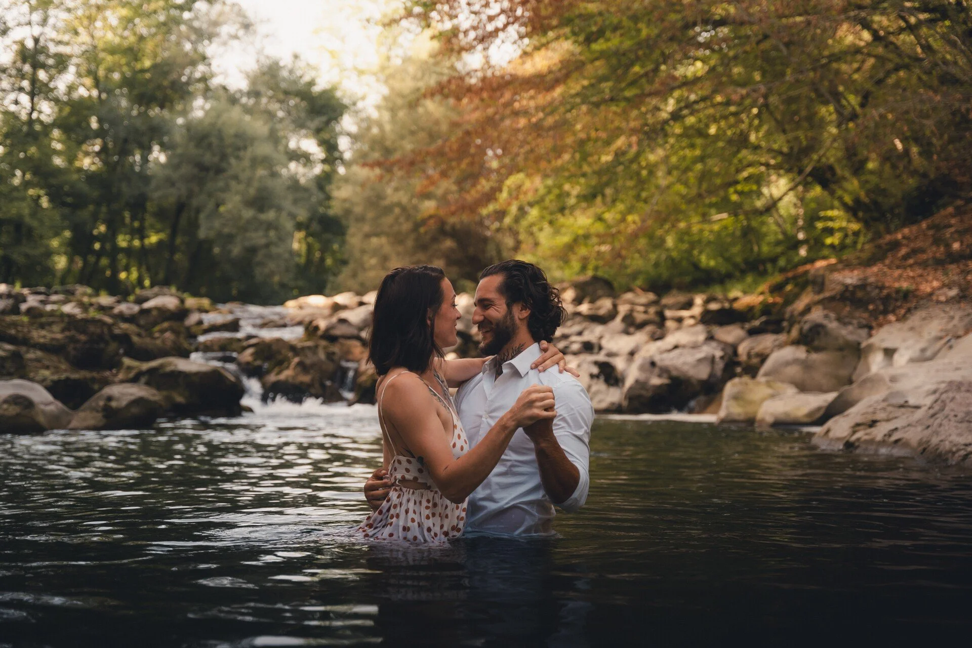 Un couple dans l'eau, échangeant un moment complice et romantique dans une rivière entourée de végétation