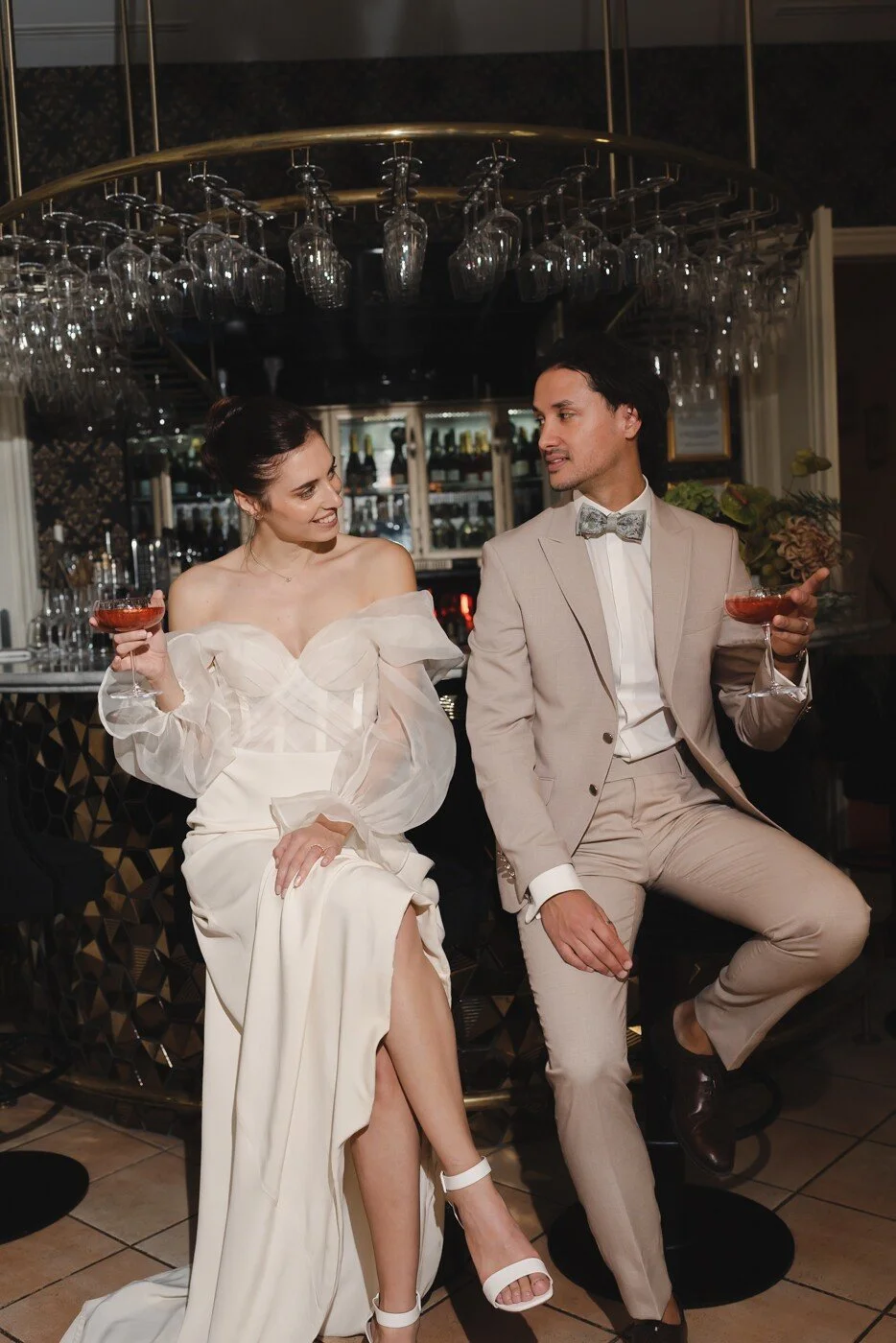 La mariée et le marié profitent d'un moment détente au bar, cocktail à la main, échangeant des regards complices.