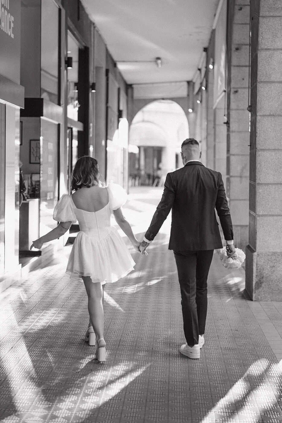 Un couple de mariés marche main dans la main sous les arcades d’Annecy.