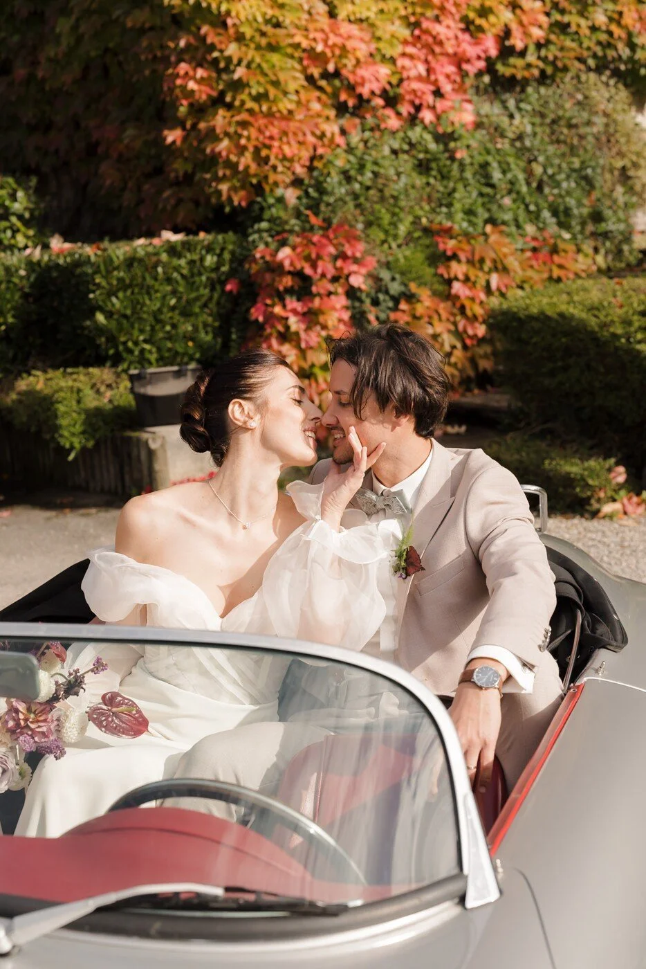 Les mariés partageant un moment complice et romantique dans une voiture vintage décapotable, évoquant un esprit d'aventure et de liberté.
