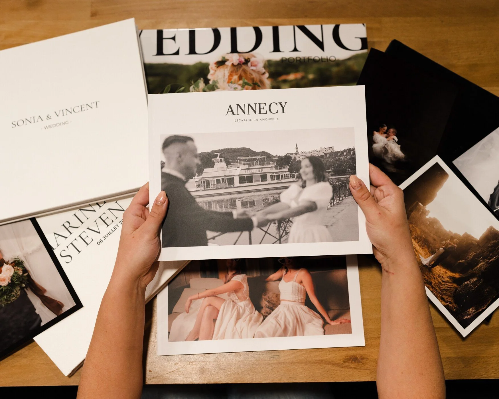 Mains feuilletant un album de mariage, entourées d'autres tirages photo et coffrets. Symbolisant la conservation des souvenirs précieux.