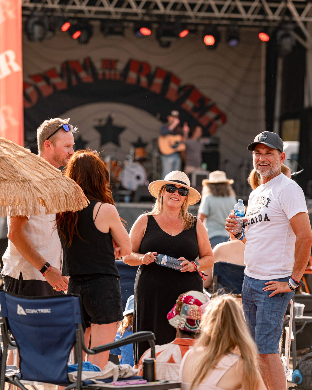 People gathered at an outdoor music concert with a band performing on stage in the background.