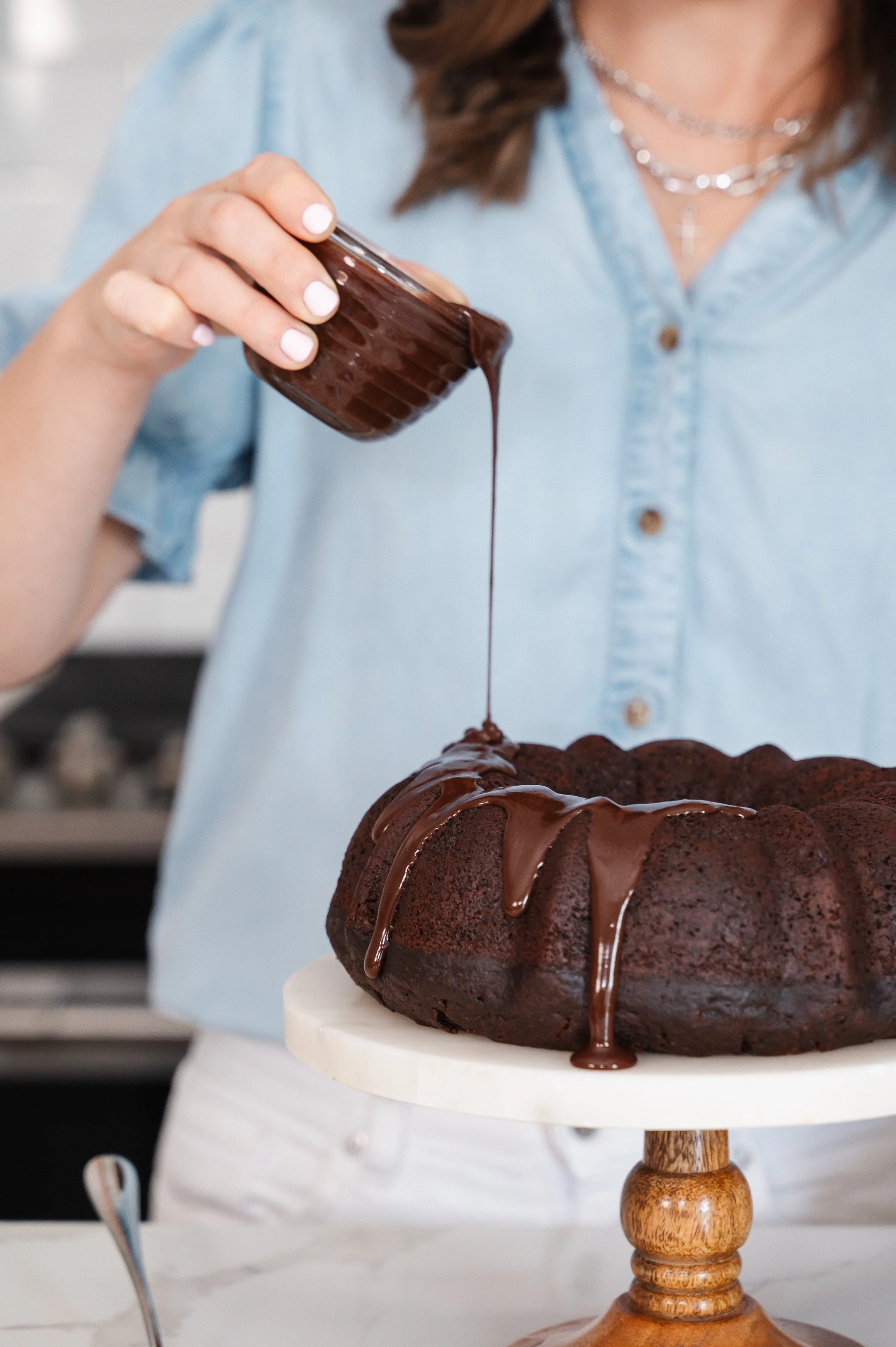 close up of female hand pour chocolate icing onto chocolate cake