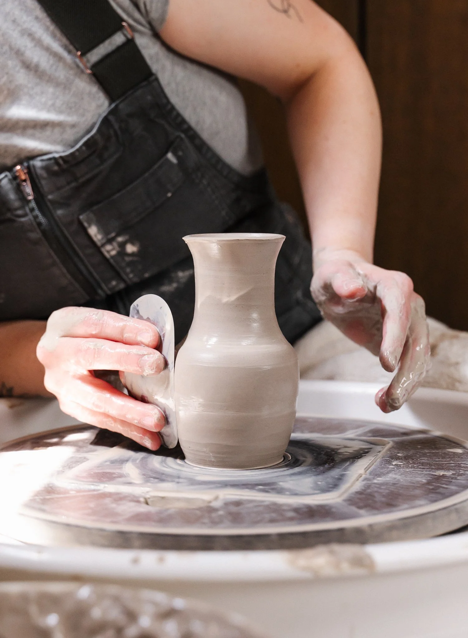 Potter's wet hands shaping a clay vase on potter's wheel