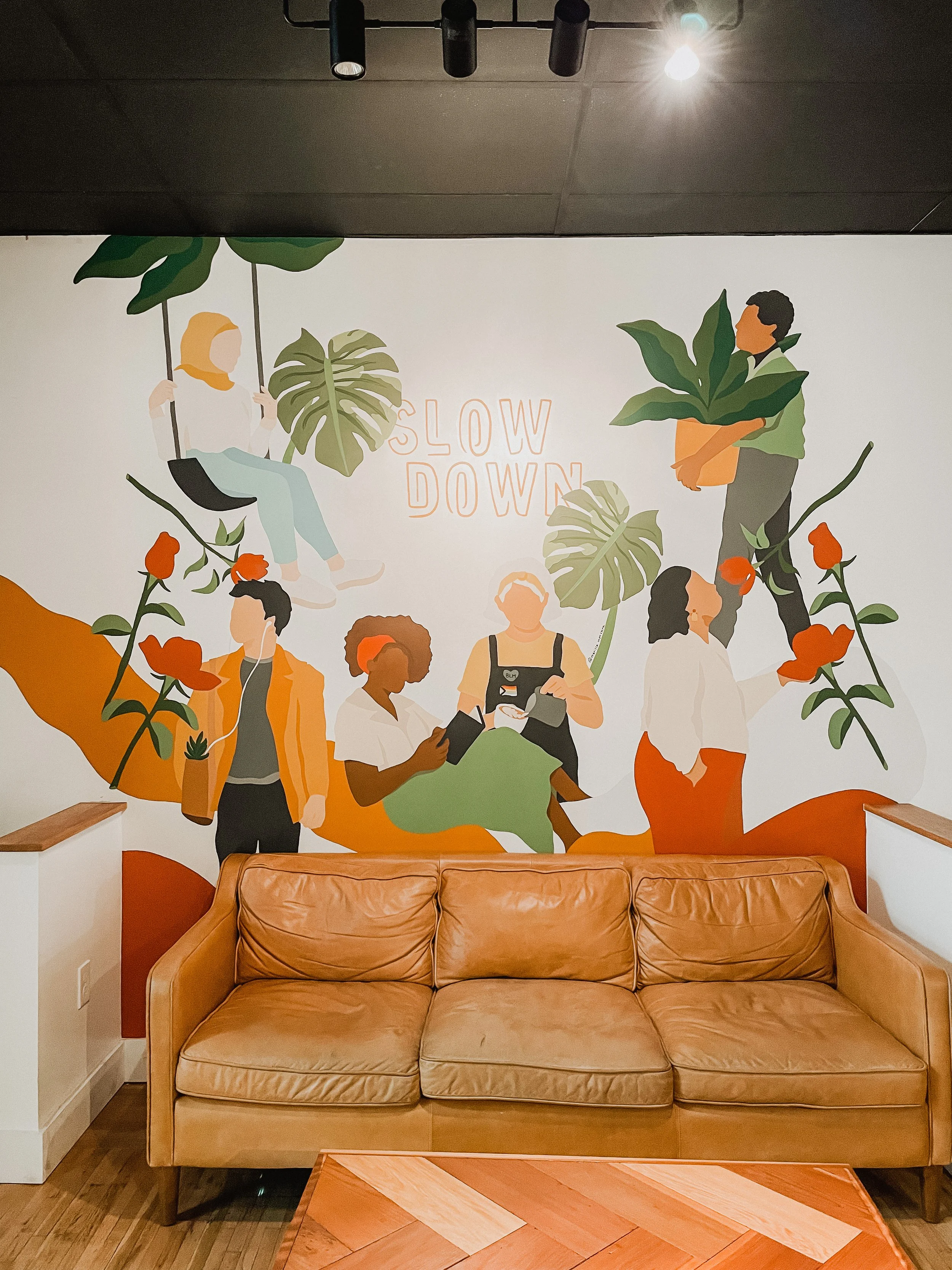 leather couch in front of Slow Down mural of people and plants