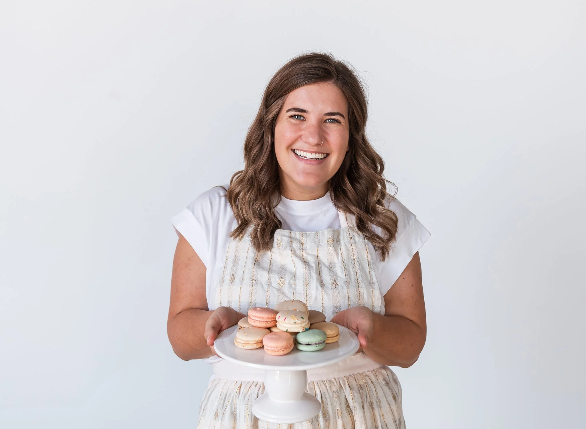 female baker wearing apron and holding platter of macarons