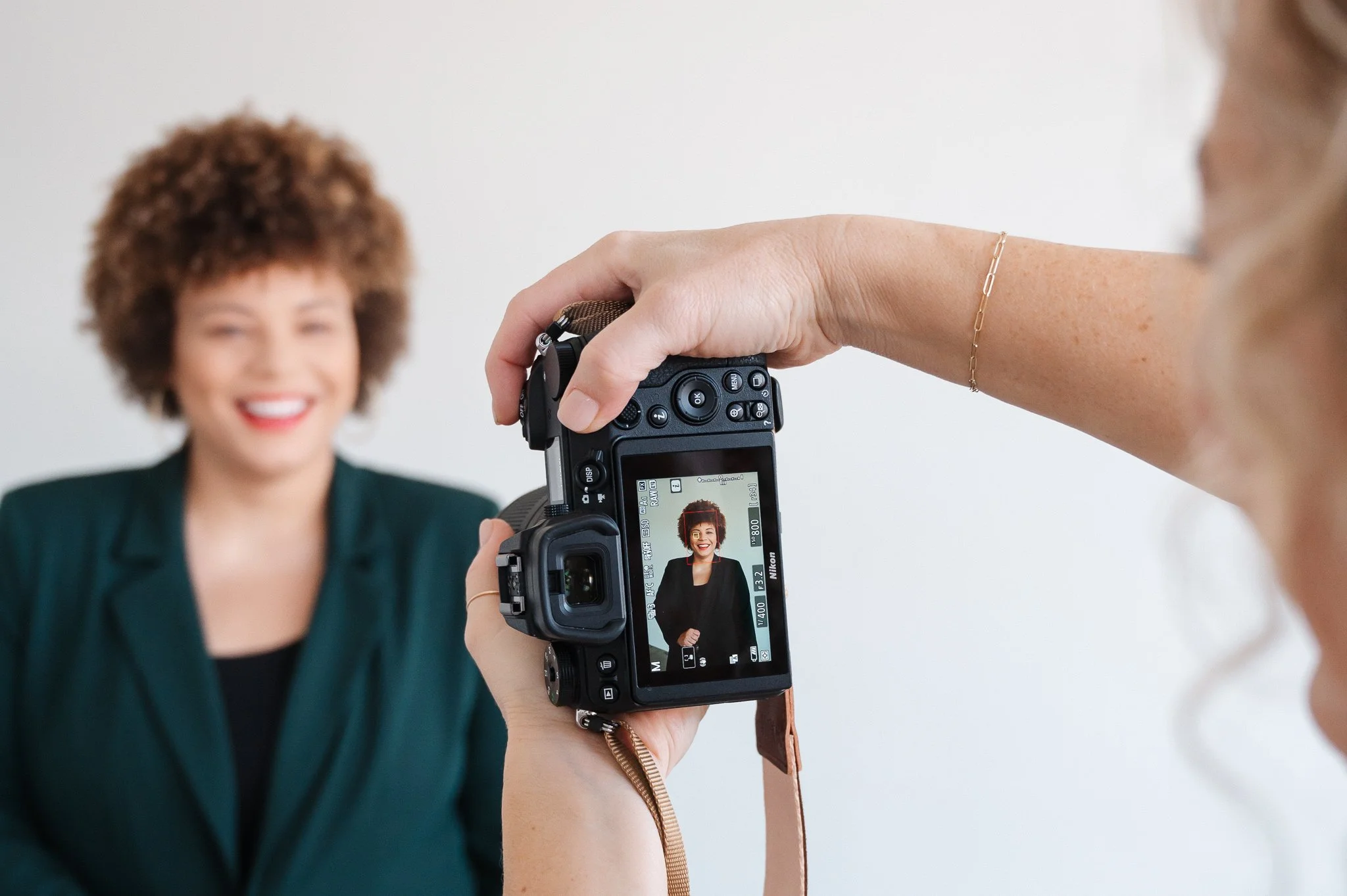 Jill holding up her camera to take a headshot of her client who is visible on the back of the camera and also in the background