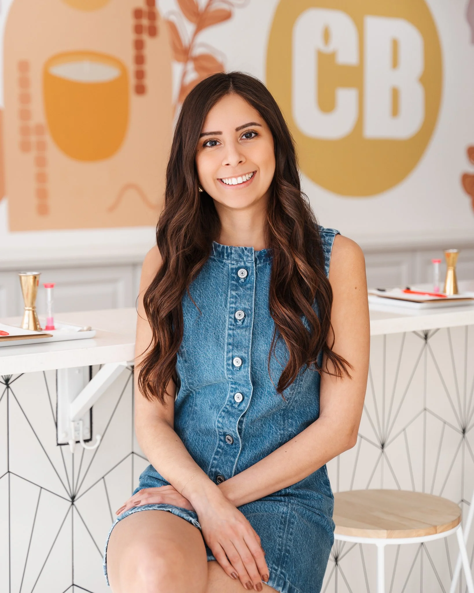 Candle Bar DSM owner Maria Abbas sitting on a bar stool in her shop smiling at the camera