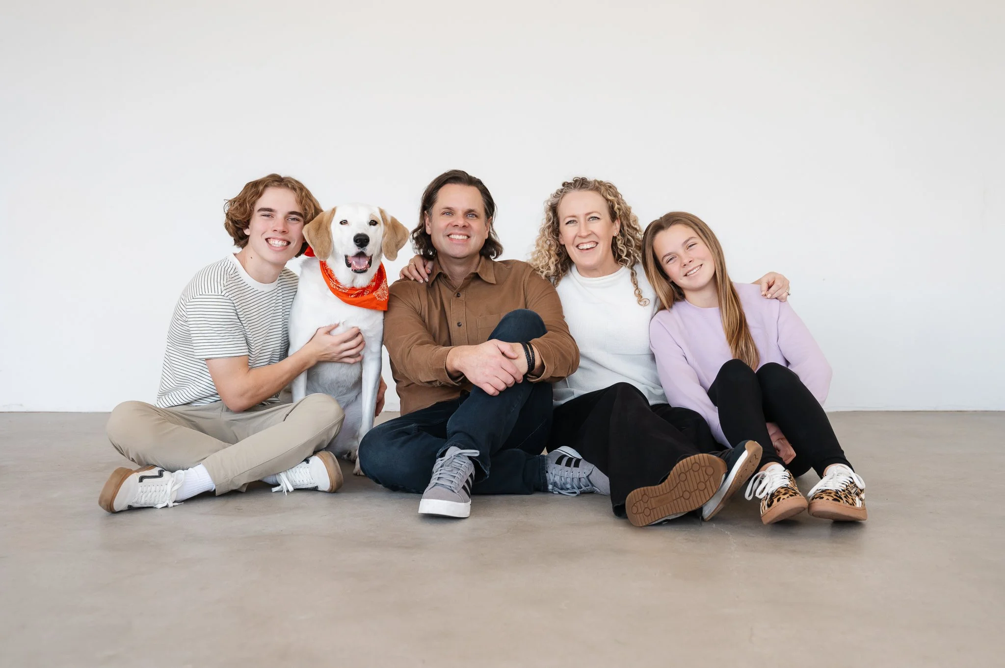 Jill Neil sitting on studio floor smiling for a posed photo with her husband, son, daughter and dog