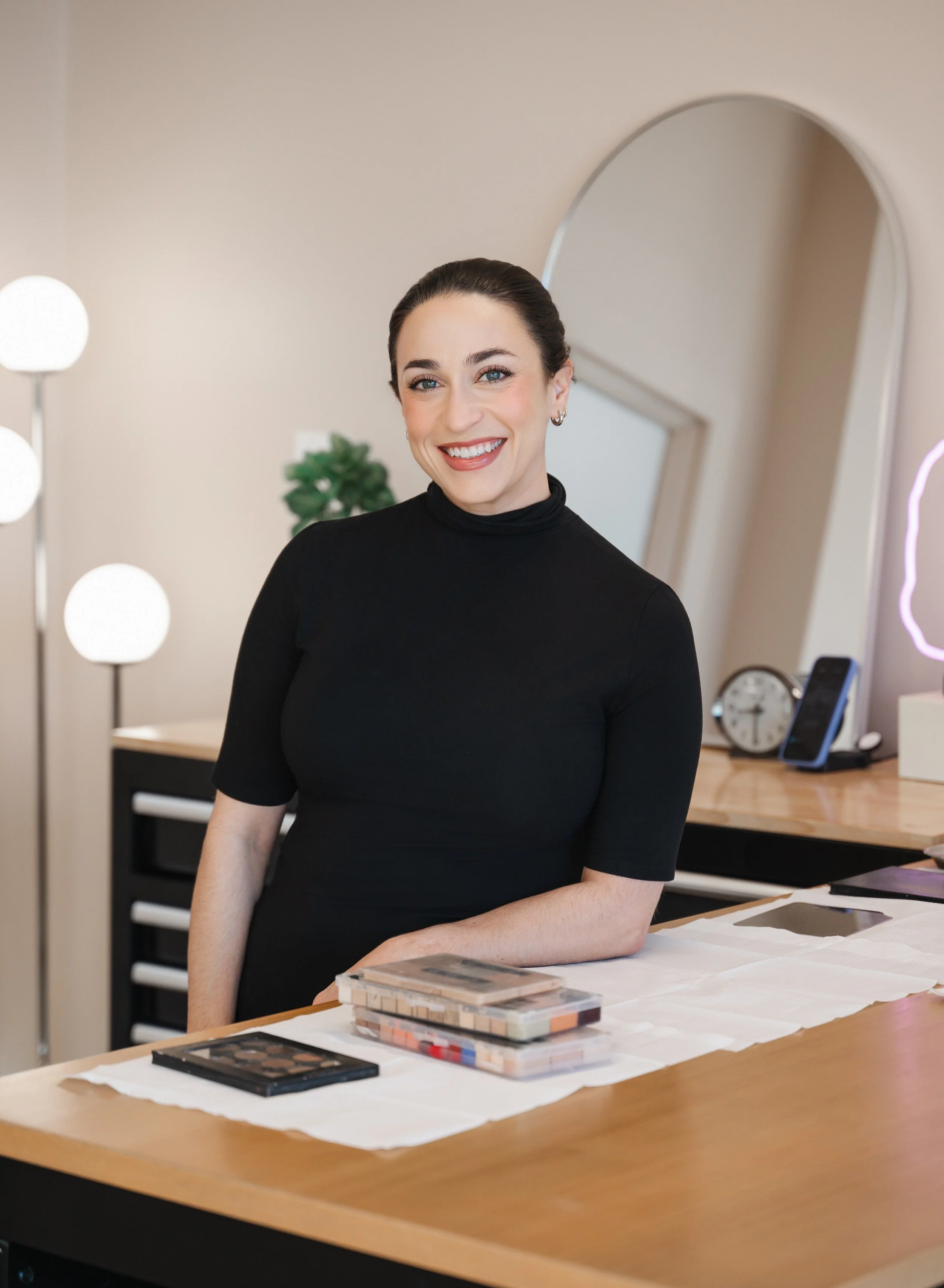 Ivy Boyd standing at makeup table smiling in her Des Moines studio