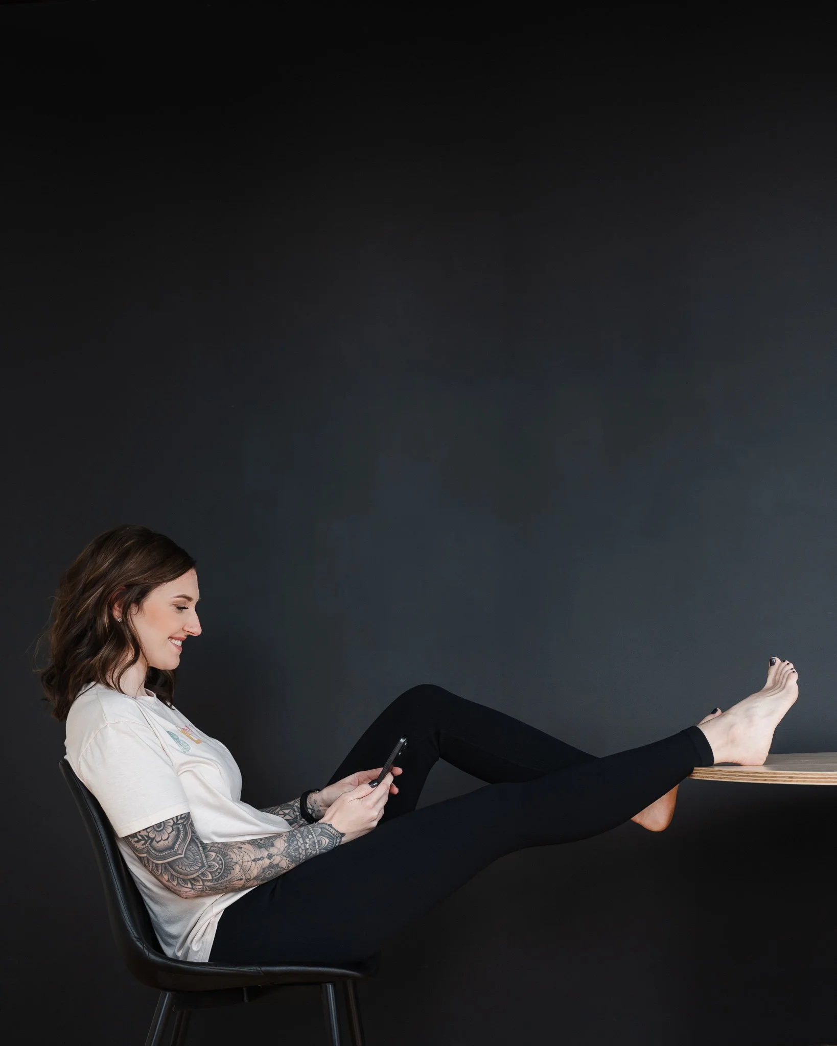 female sitting in chair with legs propped up on desk holding cell phone and smiling