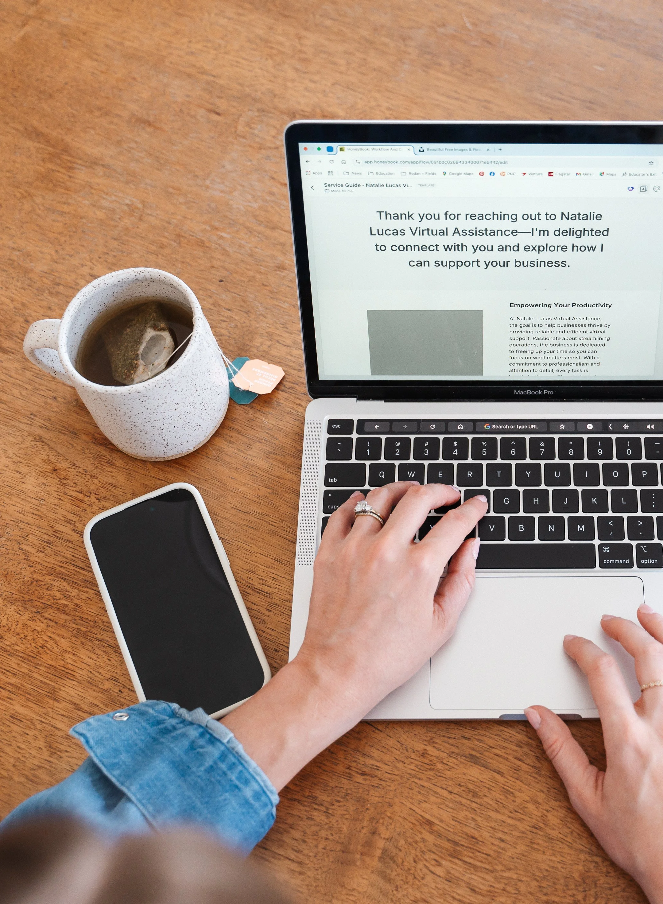 close up of female hands typing on laptop with a mug of tea and cell phone on table top