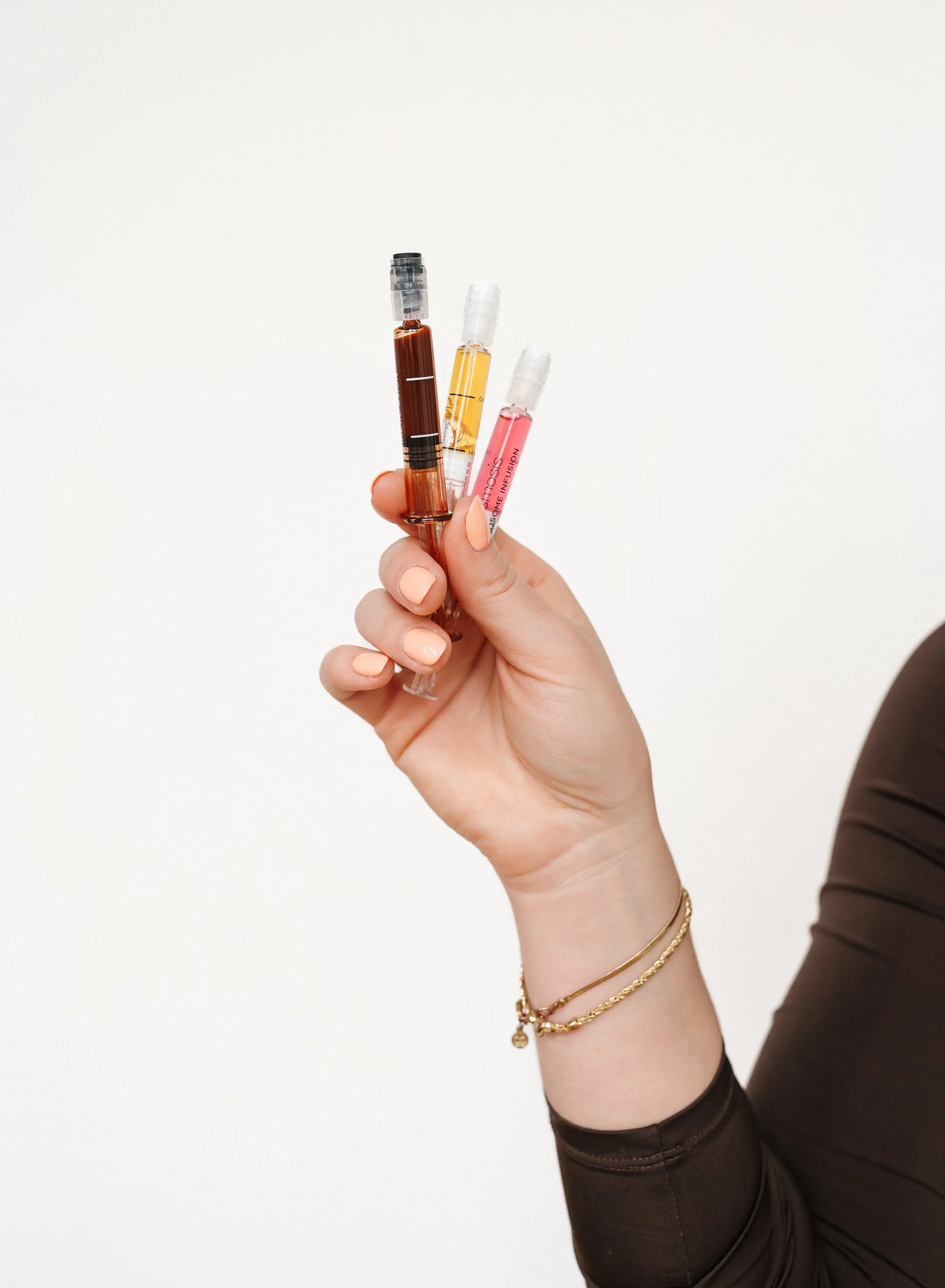 Close up of female hand holding three colorful vials of cosmetic injectables