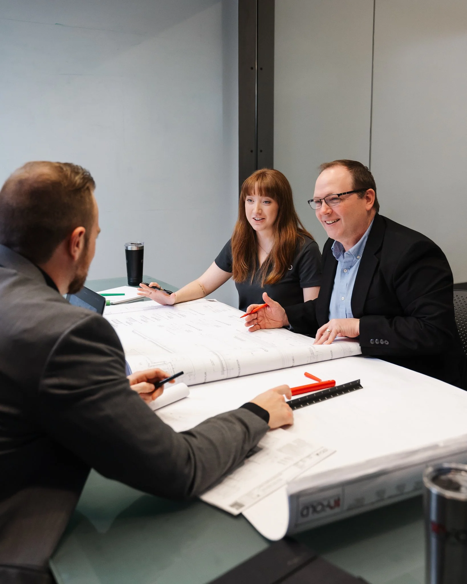 three team members sitting in conference room discussing the blue prints on the table between them
