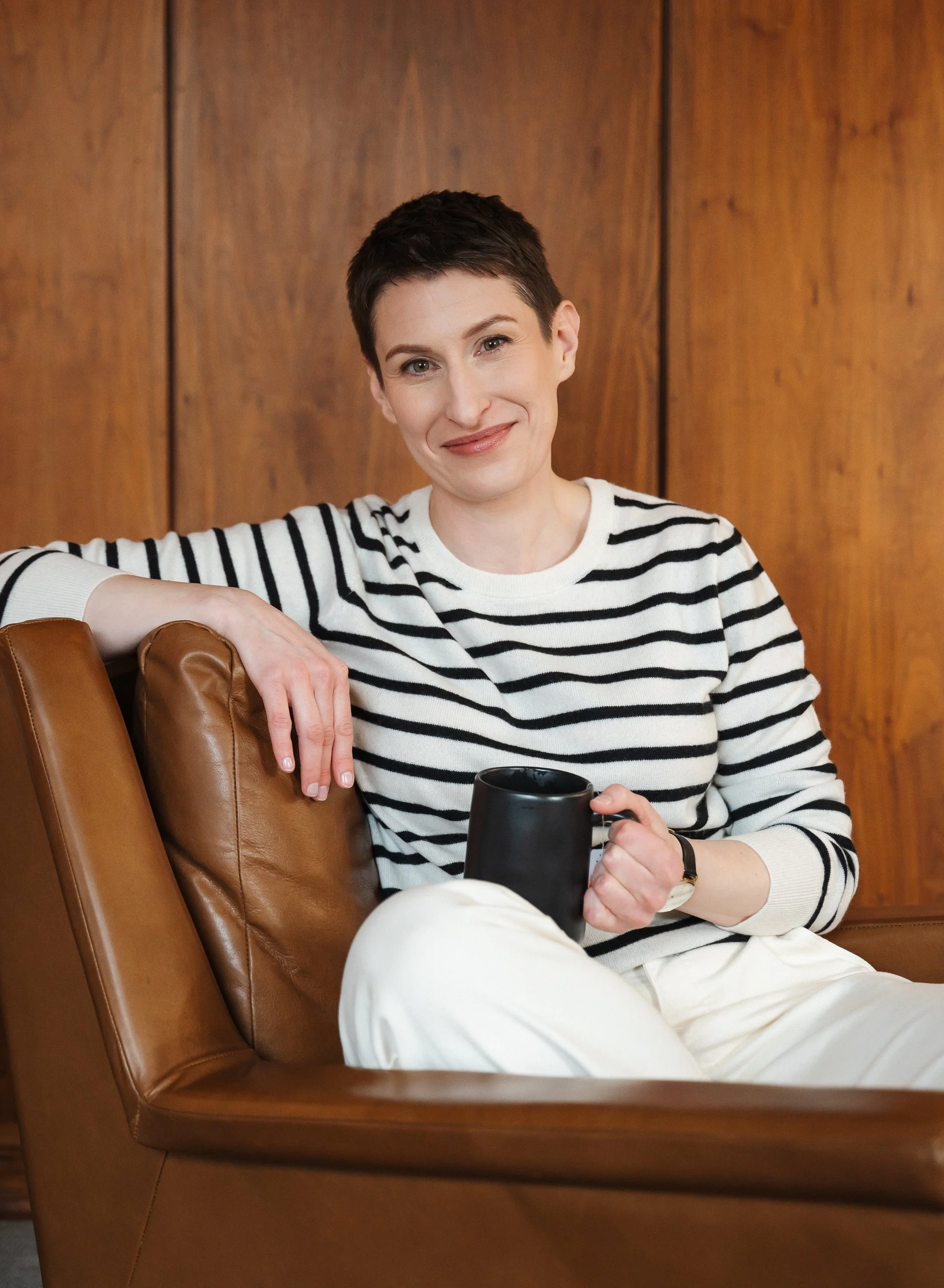woman with short hair, smooth skin and natural looking makeup smiling softly in chair