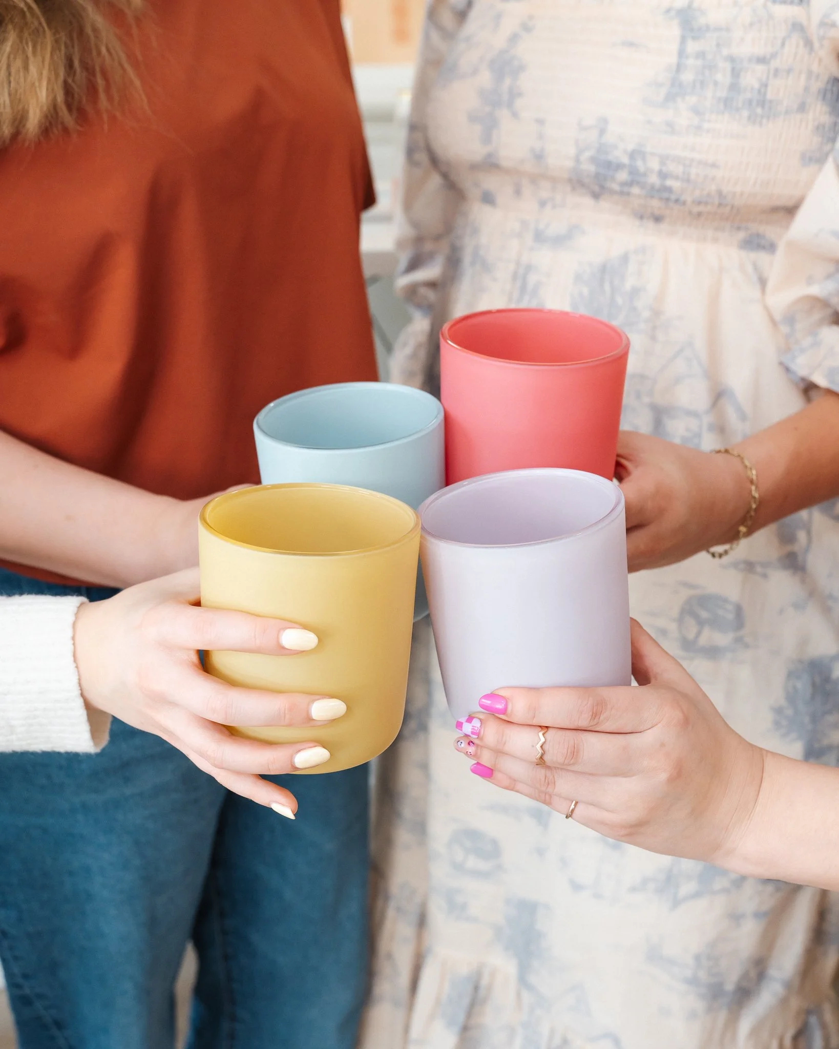 four arms each bringing a different color of candle vessel together in a cheers