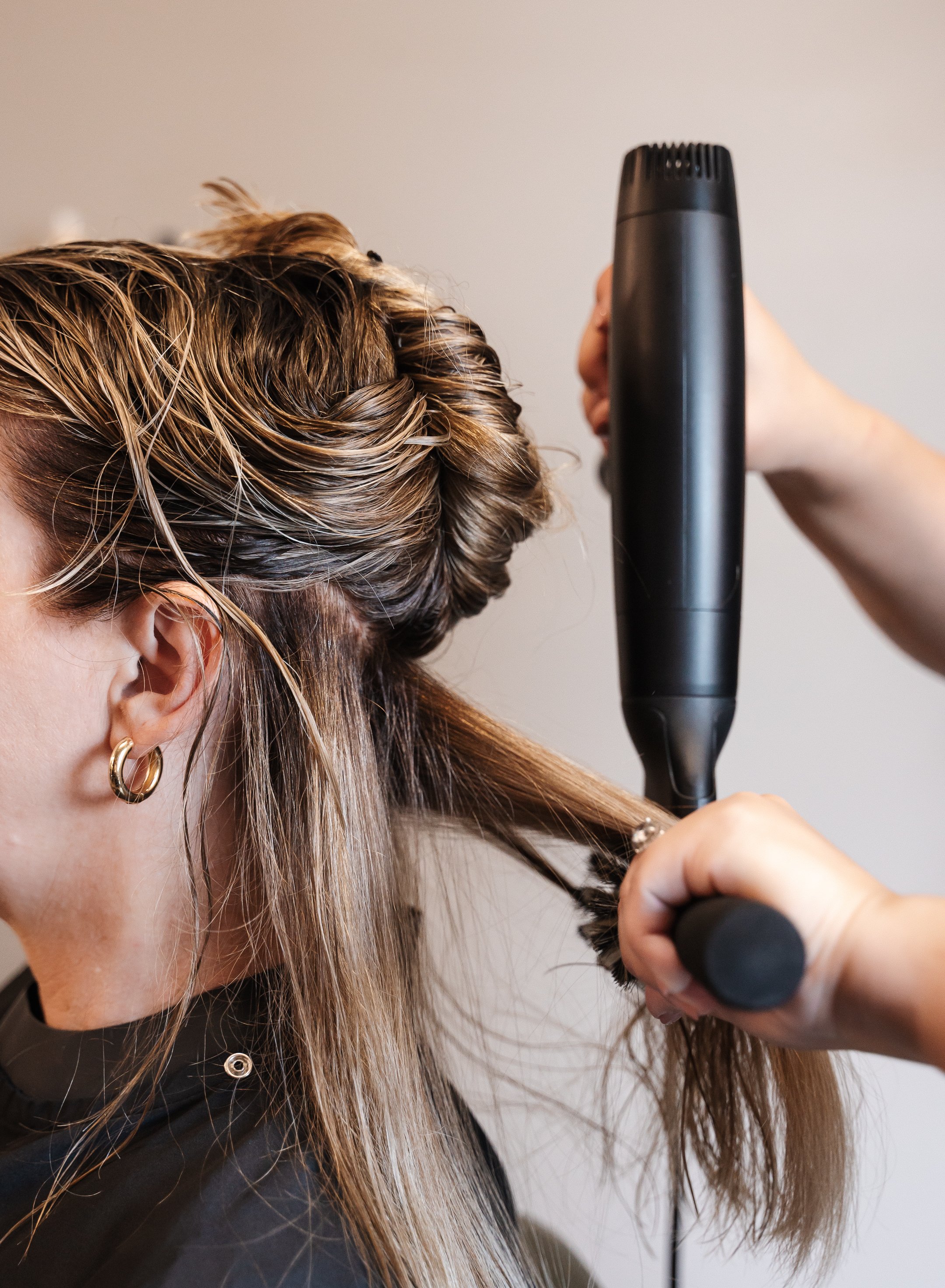 Close up profile of a hair stylist drying a female client's long hair with a hair dryer and brush