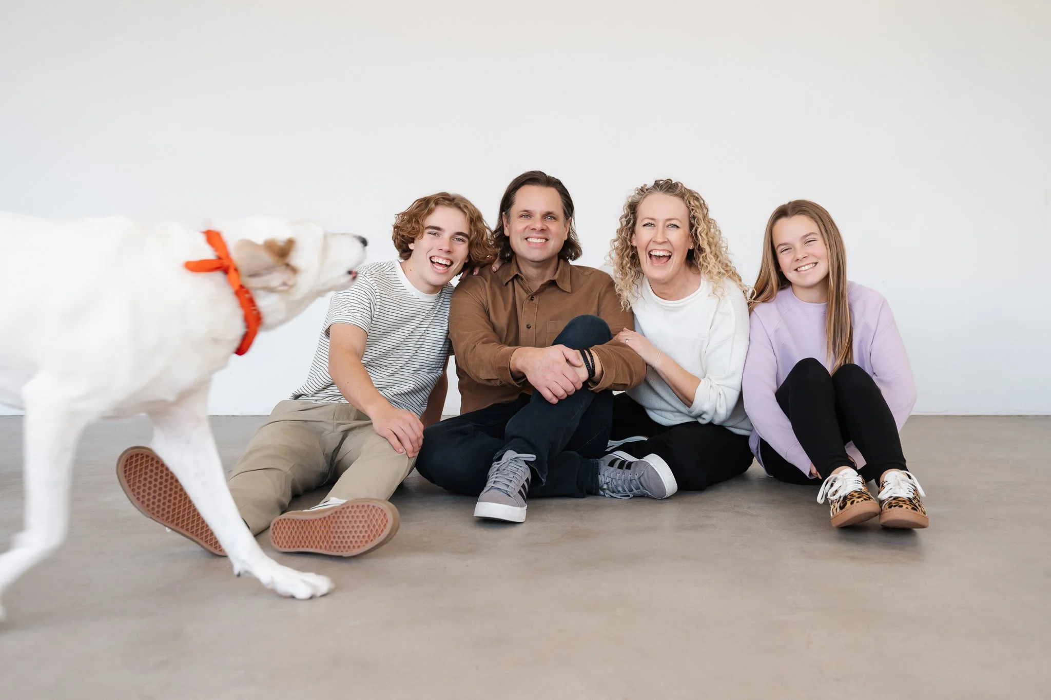 Jill sitting on studio floor laughing with her husband, son and daughter while their dog runs into the frame