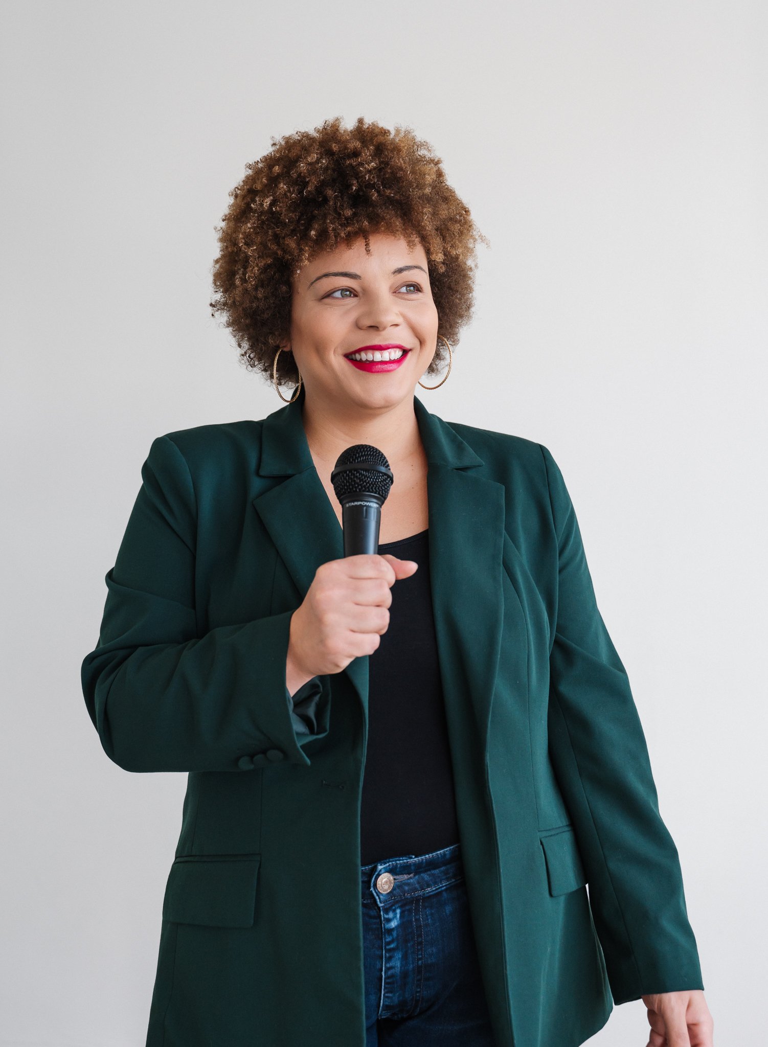 woman in blazer holding microphone and smiline