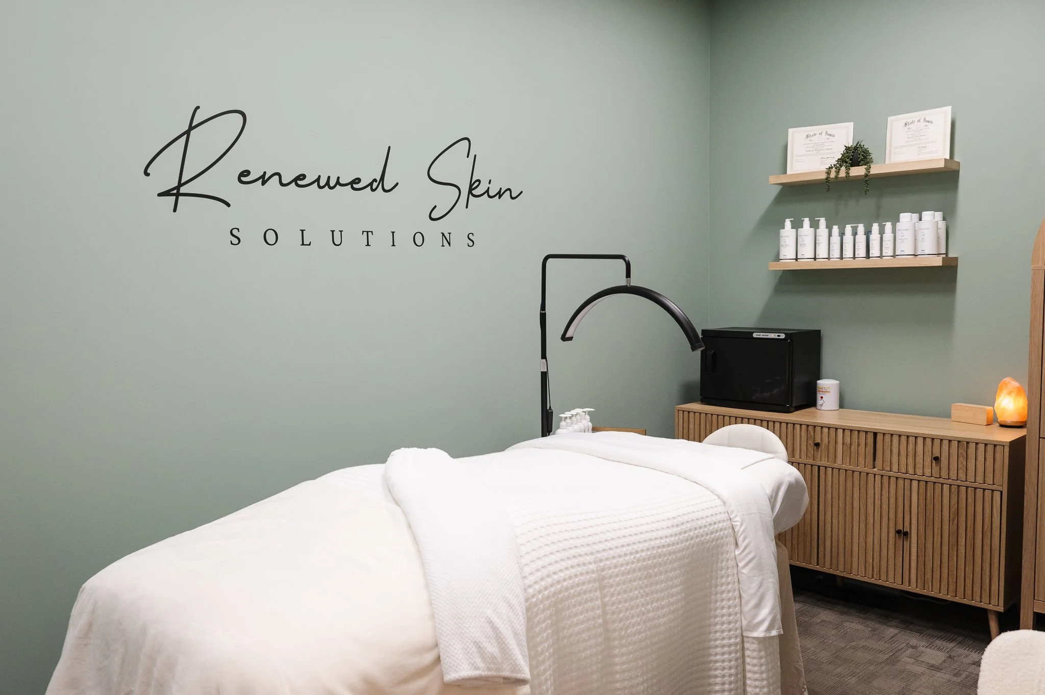 esthetician facial room in a calm sage green with Renewed Skin Solutions logo on wall