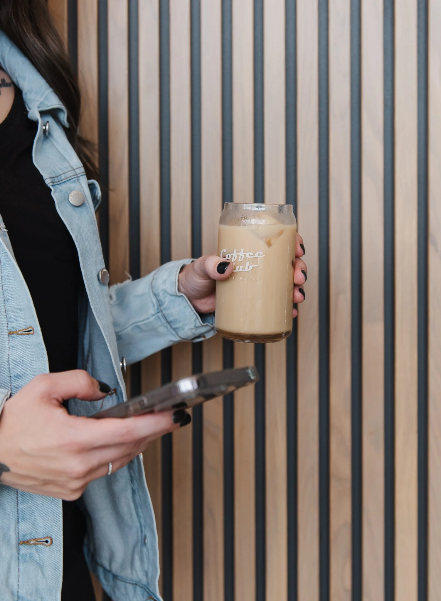 Close up of female hands holding an iced coffee in one hand and her cell phone in other