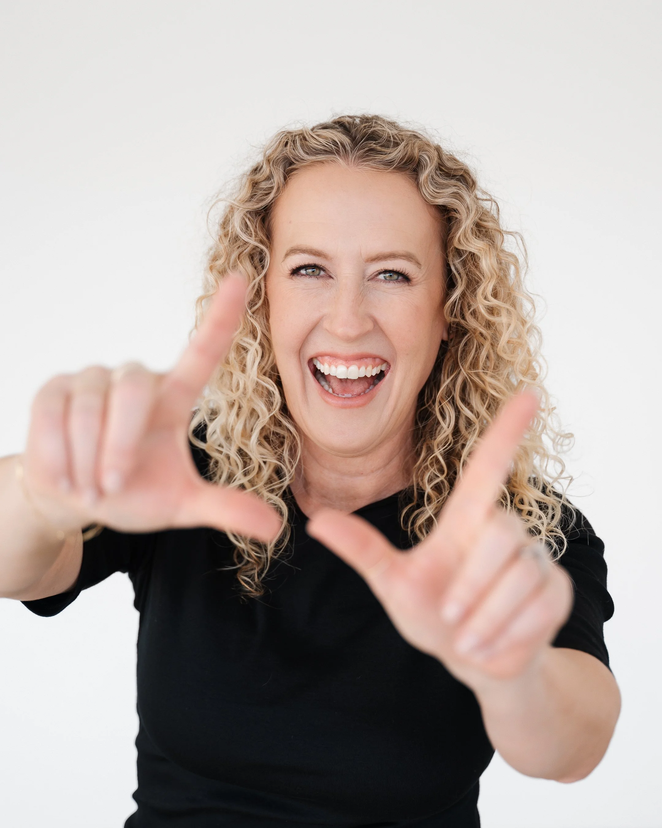 Jill laughing while holding up her hands in an L shape to frame her face like a photograph