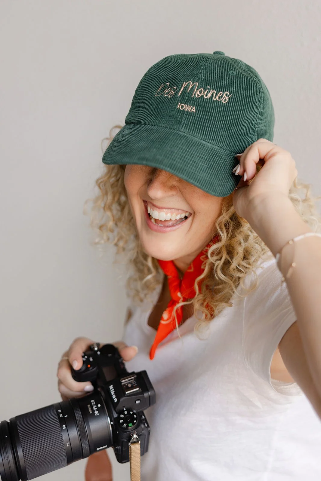 Jill Neil holding camera and laughing as she pulls her Des Moines embroidered baseball cap down over her eyes