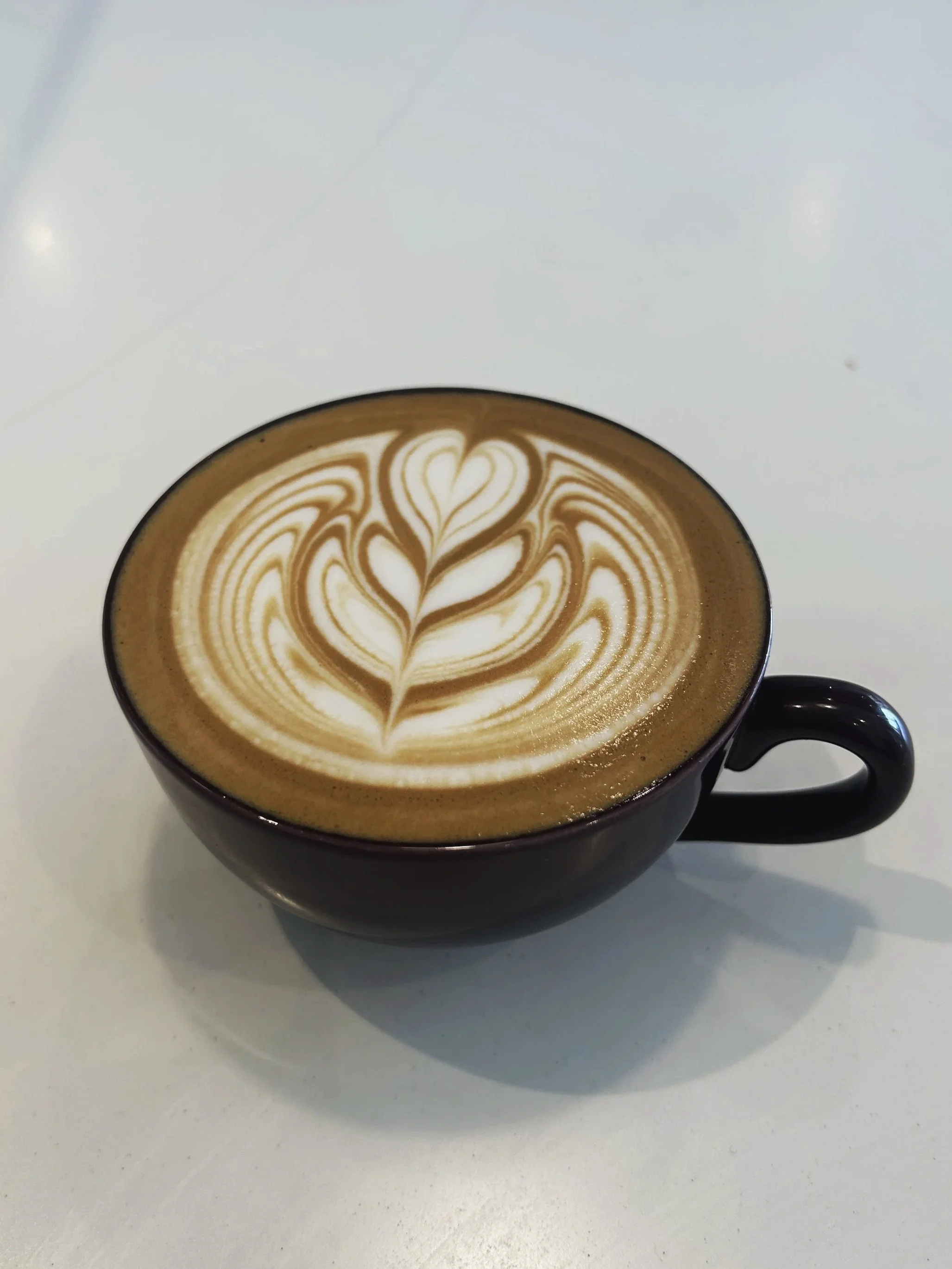 Black coffee mug with intricate latte art design on coffee latte, placed on a white surface