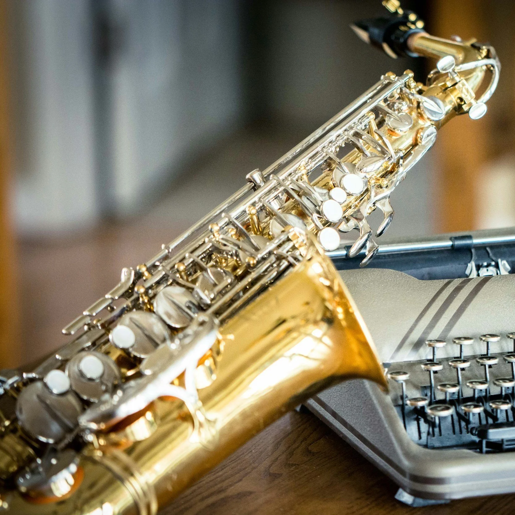 Close-up of a saxophone placed next to an old-fashioned typewriter on a wooden surface.