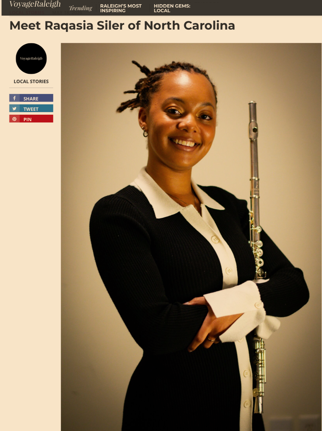 A woman smiling and holding a flute, dressed in a black and white outfit, standing against a neutral background.