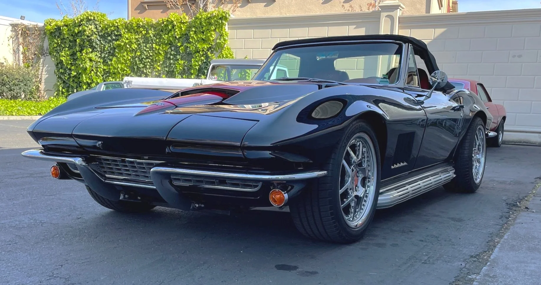 A black vintage Chevrolet Corvette Stingray convertible parked on a street with other classic cars in the background.
