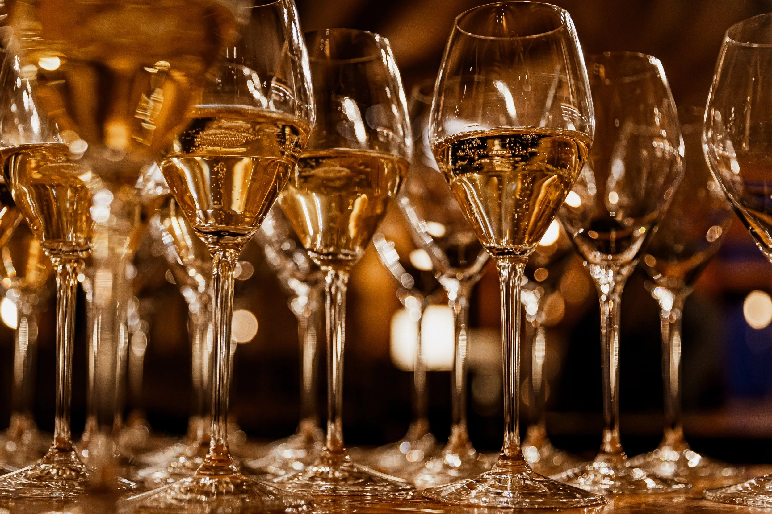 Multiple champagne glasses filled with sparkling wine, arranged on a table in a dimly lit setting.